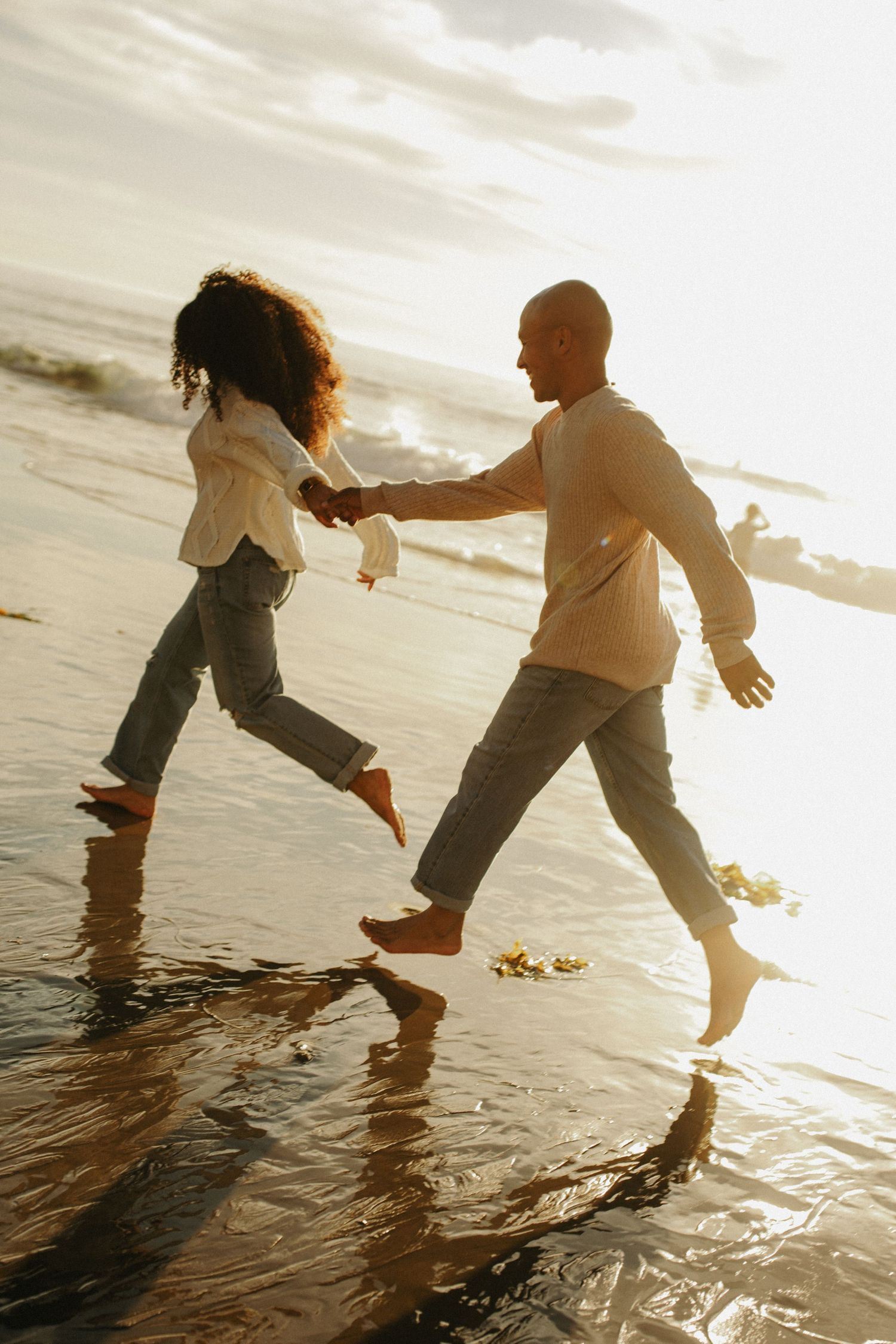 Silhouettes of people splashing and playing in shallow ocean water at sunset.