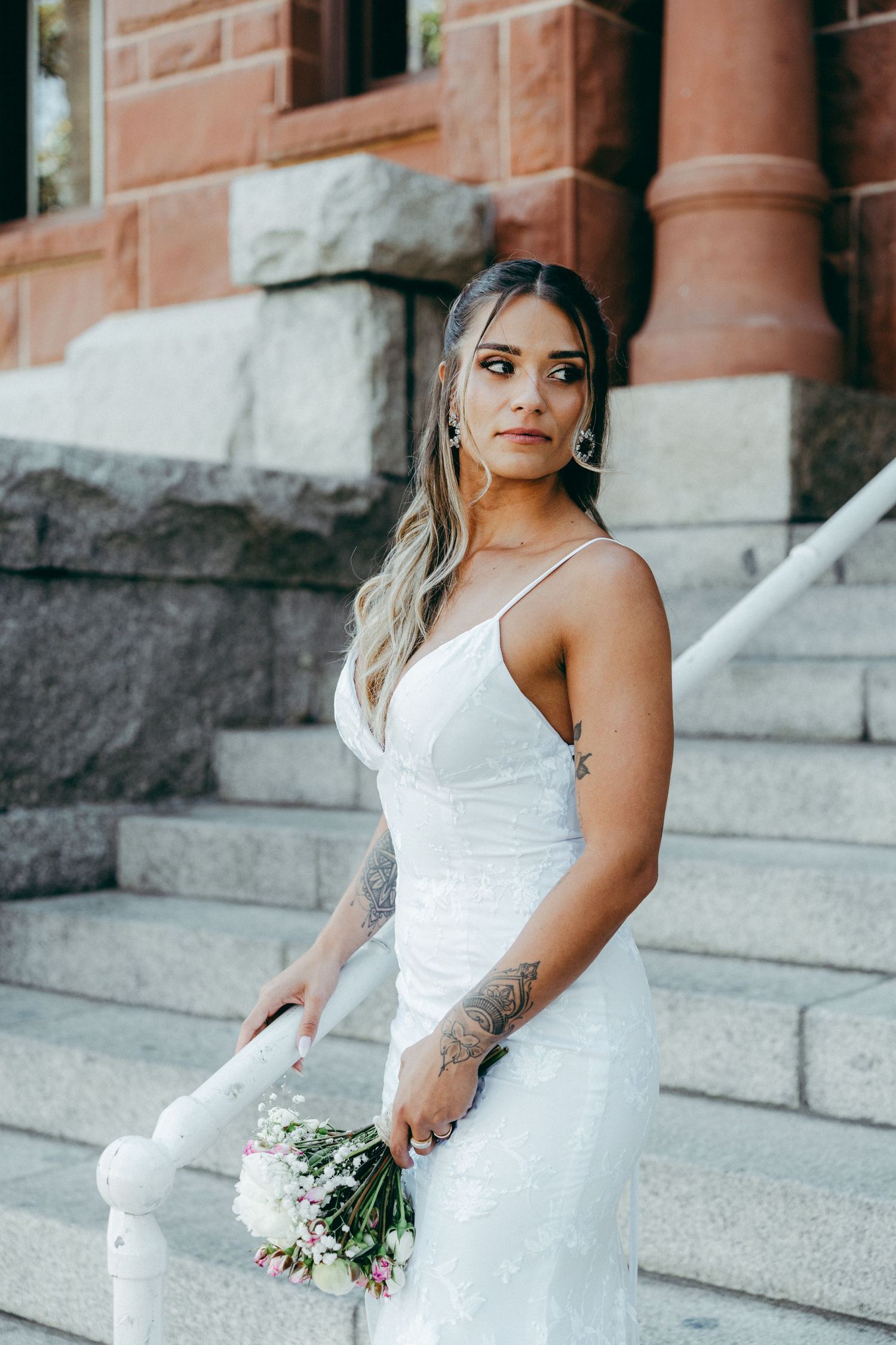 A bride in a white dress holds a bouquet while posing on stone steps.