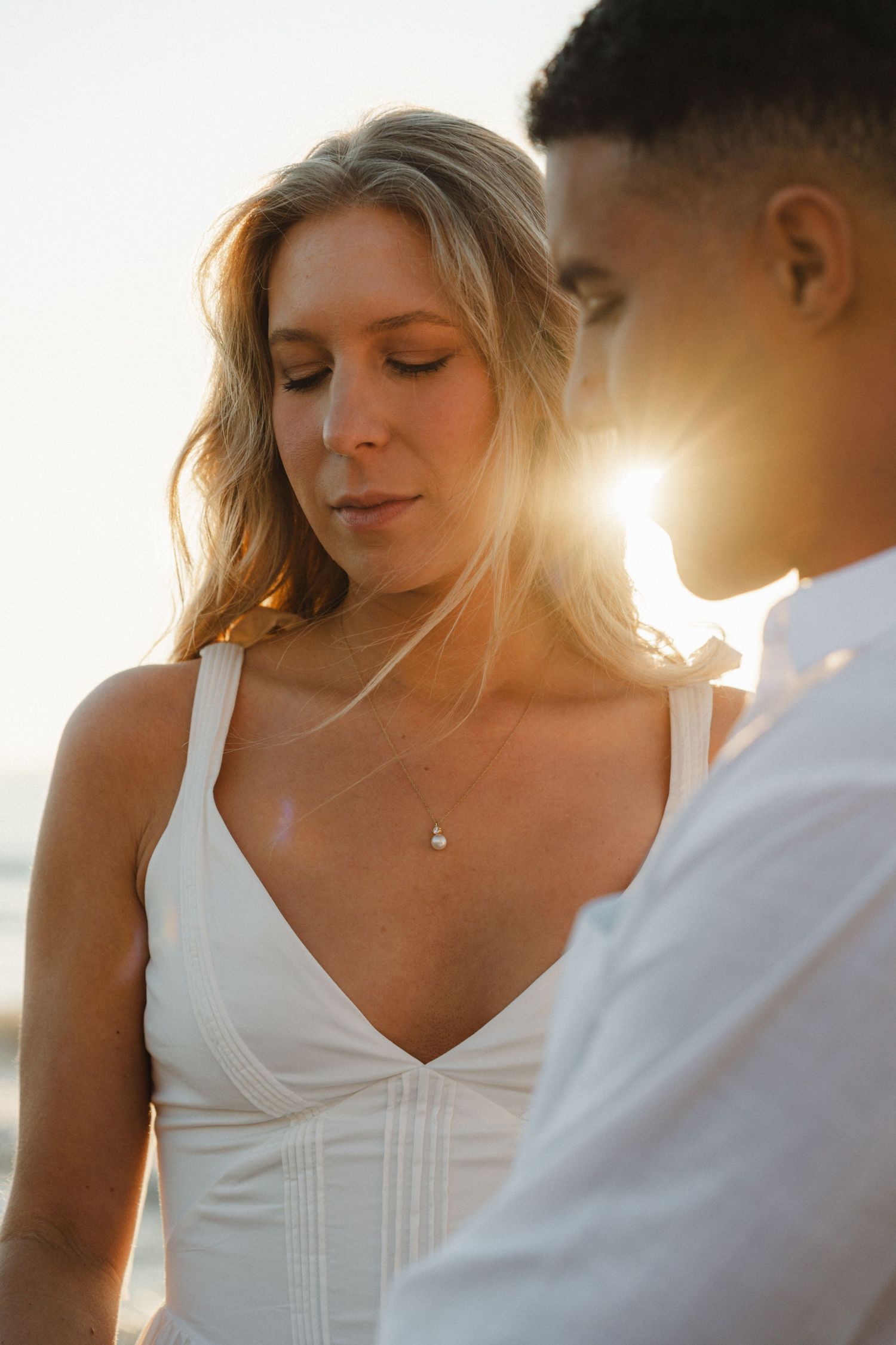 A romantic couple shares an intimate moment in warm sunlight with the bride wearing a white dress.