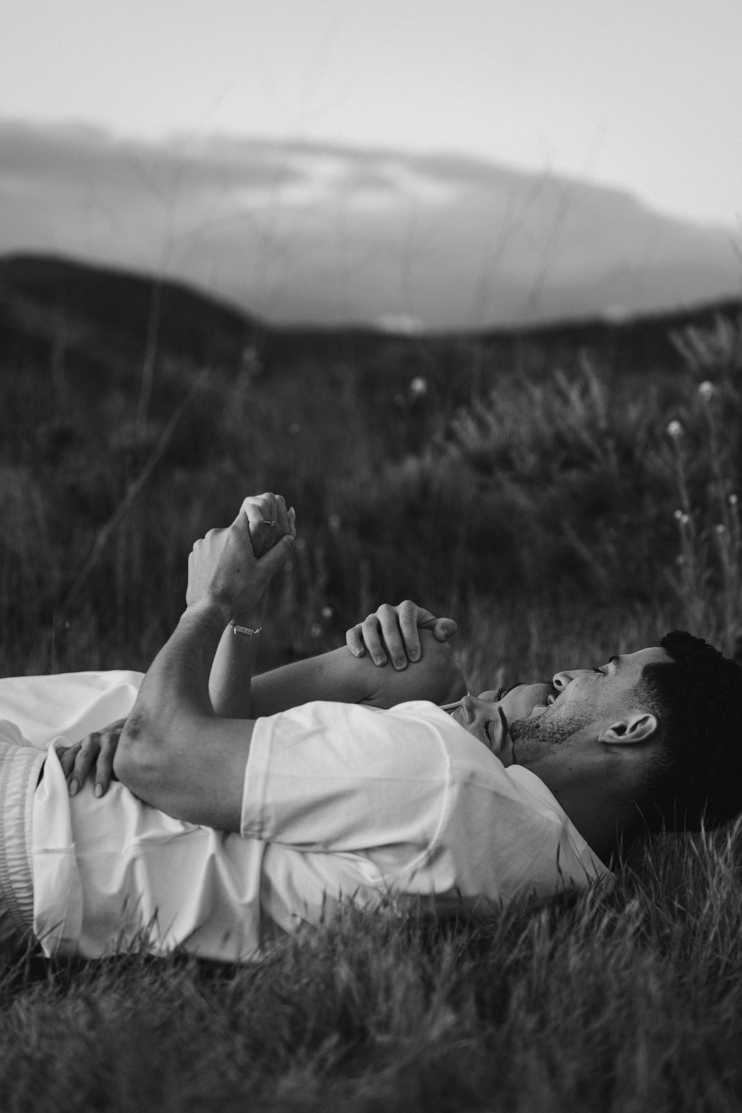 Black and white panoramic photo showing someone resting peacefully in tall grass on a hillside.