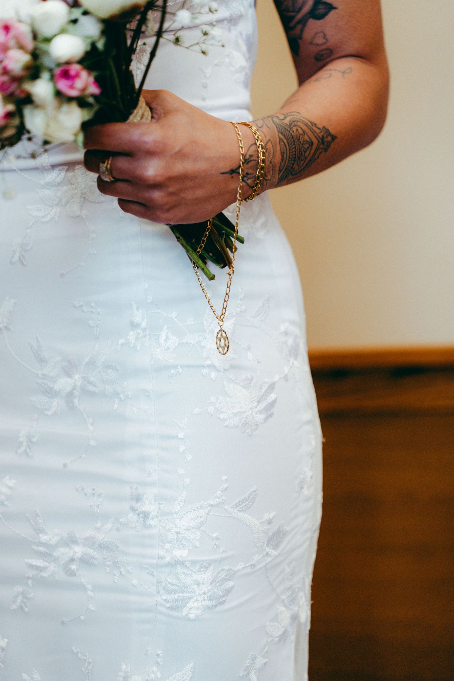 Detail shot of white lace wedding dress with floral bouquet and tattooed arm.