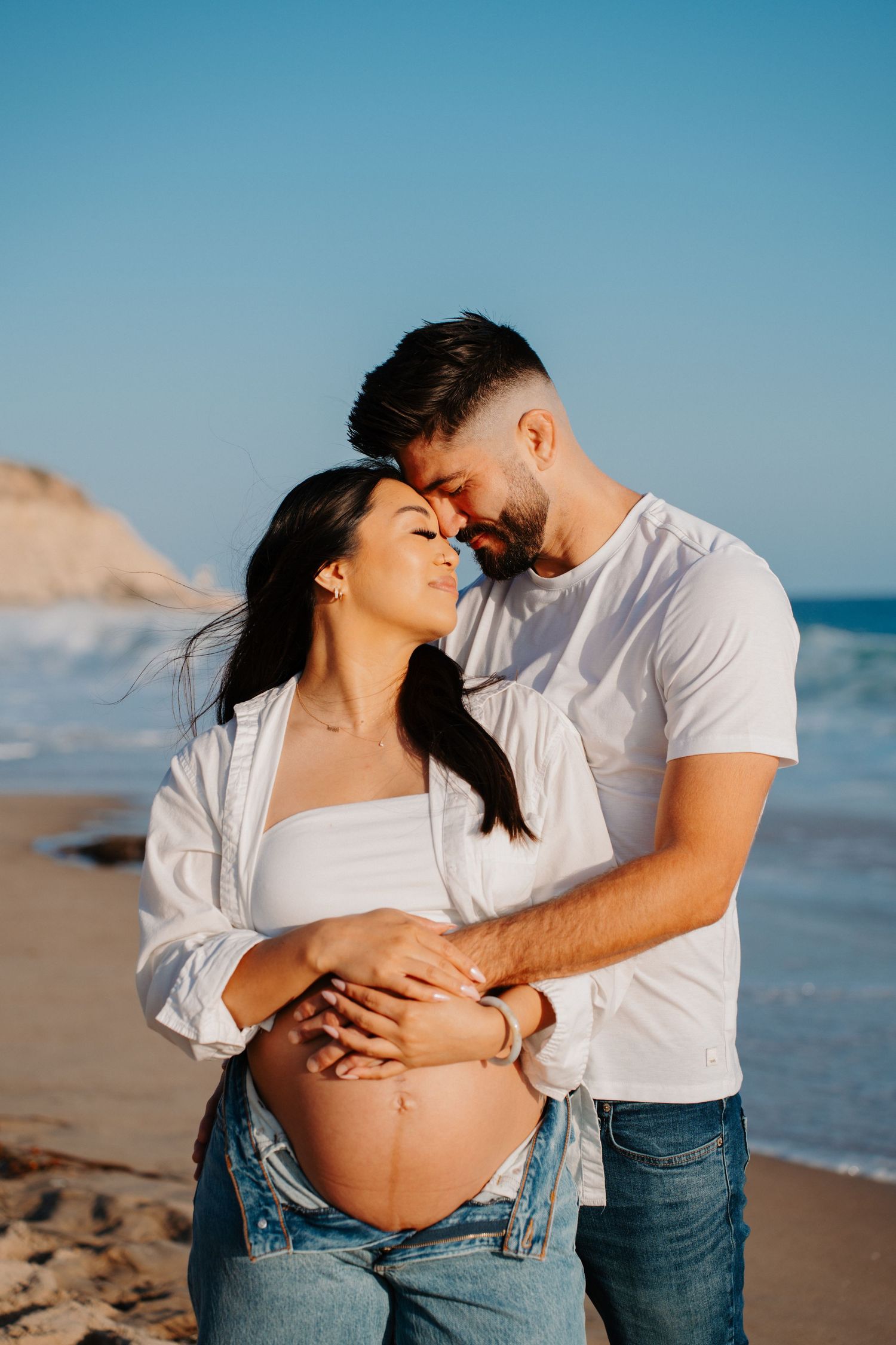 An expectant couple embraces on a beach during their maternity photoshoot at sunset.