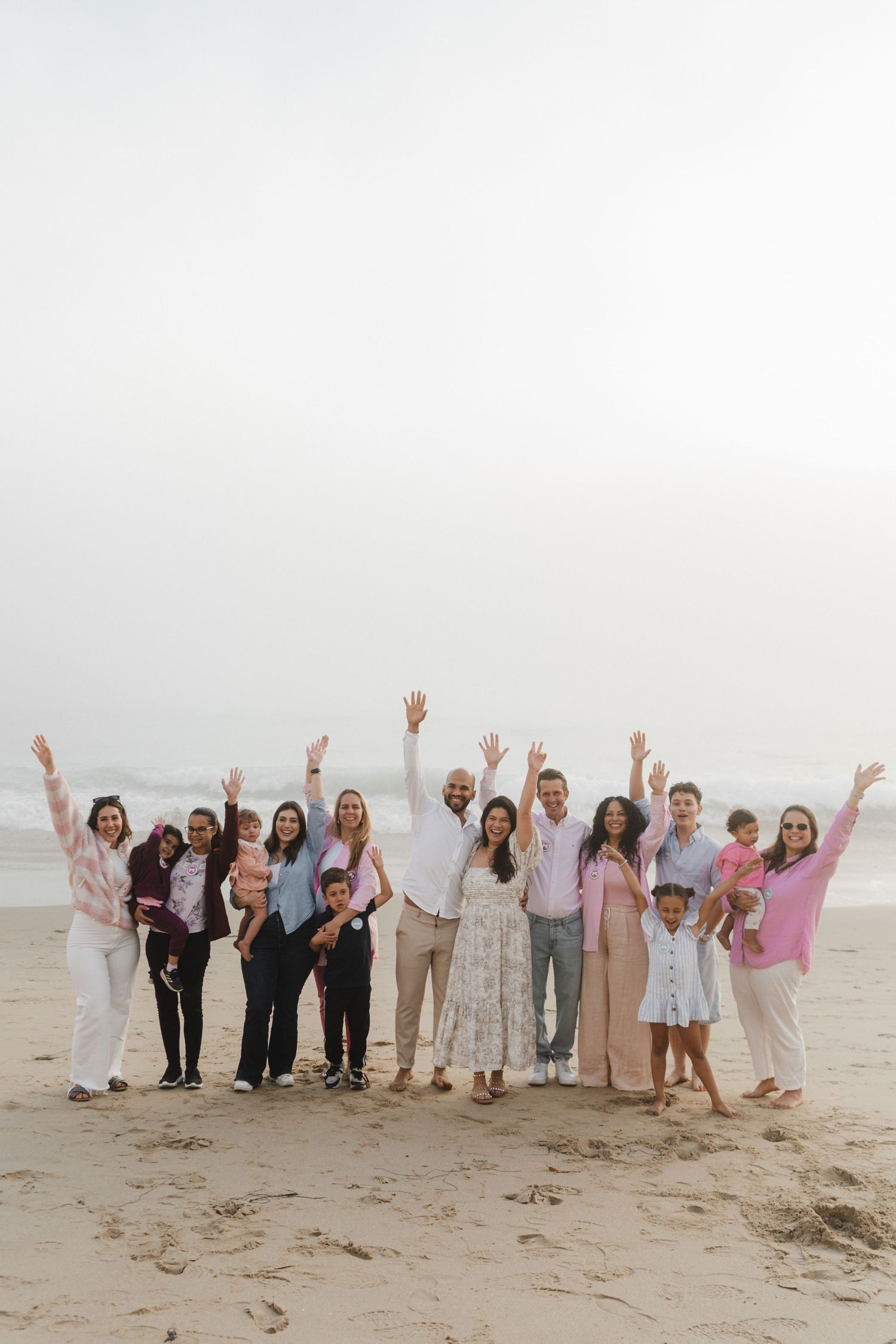 A celebratory group photo of people with raised arms on a misty beach.