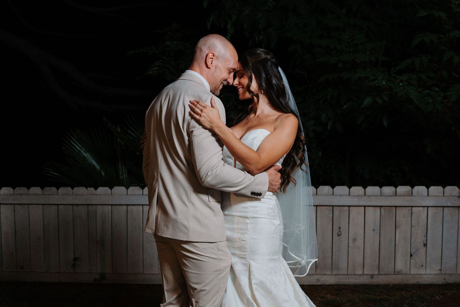 Wedding couple embracing in romantic outdoor setting at dusk.