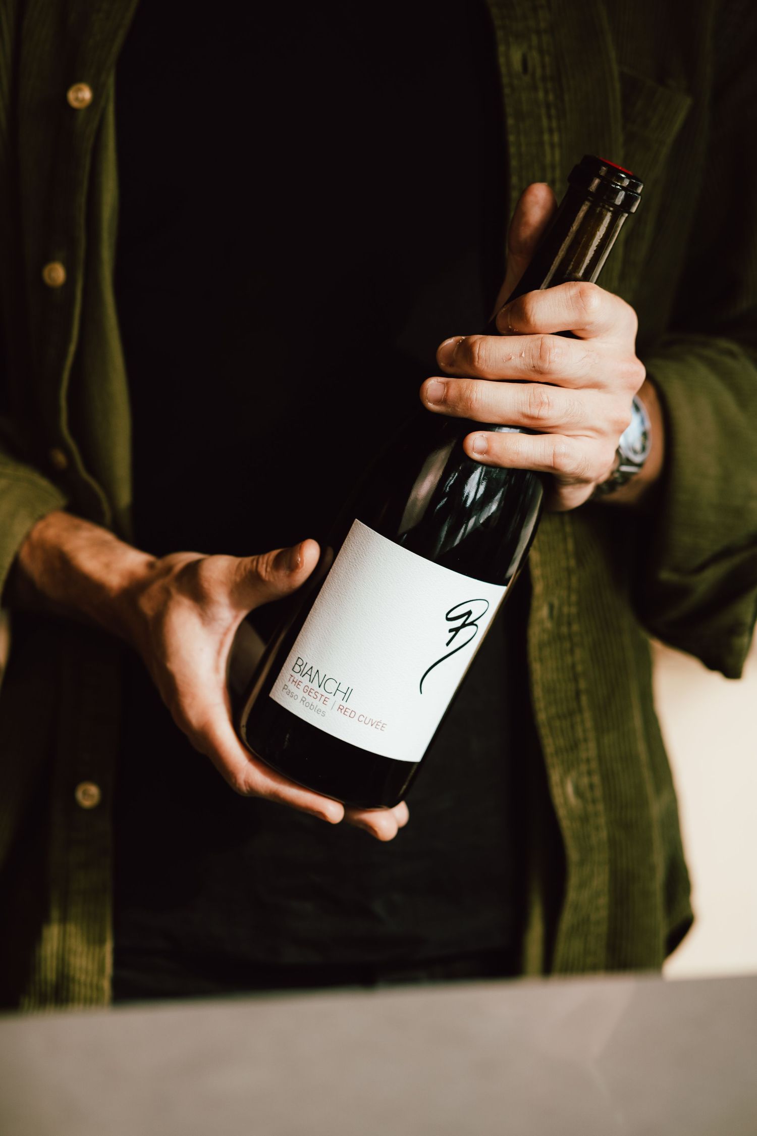 Hands holding and examining wine bottle in dark moody lighting.