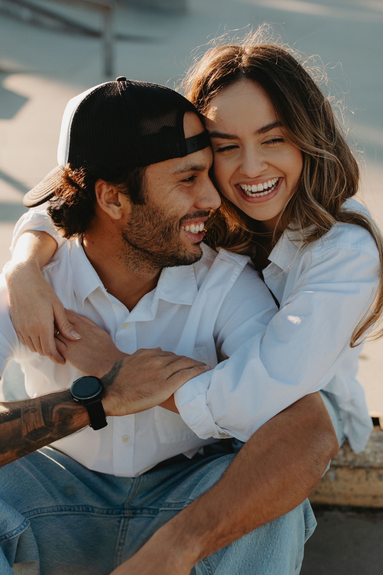 Candid outdoor photo of a couple sharing intimate laughter while wearing casual white shirts and denim.