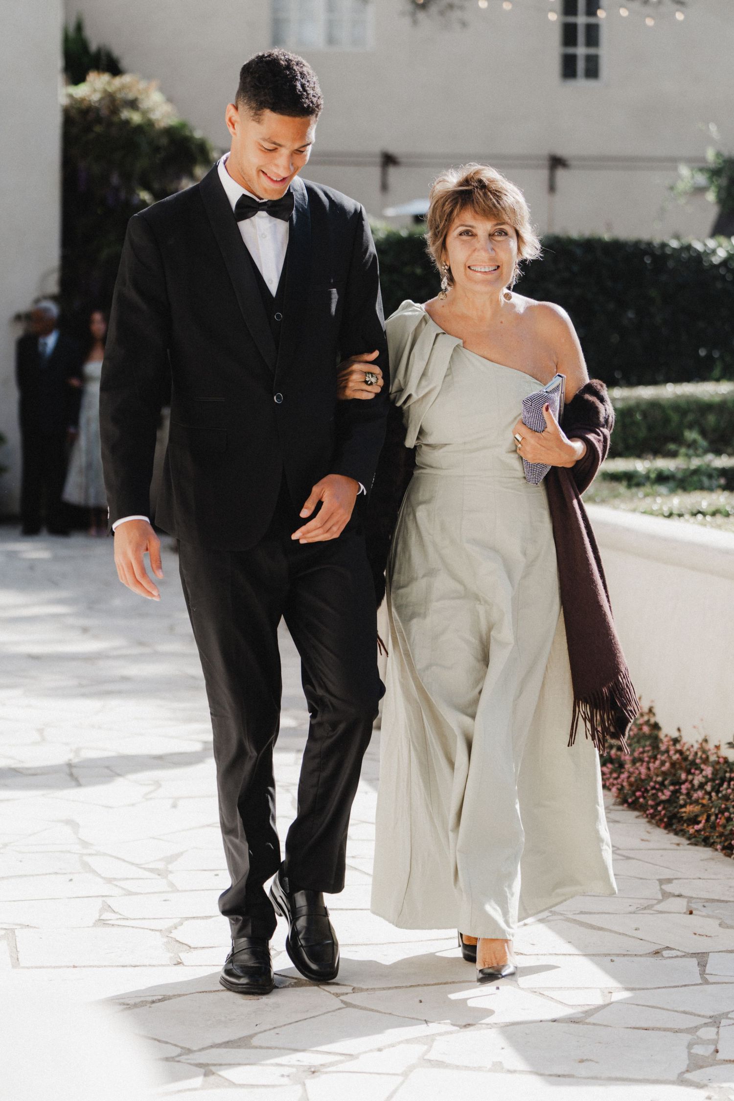 A couple walks together on white stone pavement during a formal event.