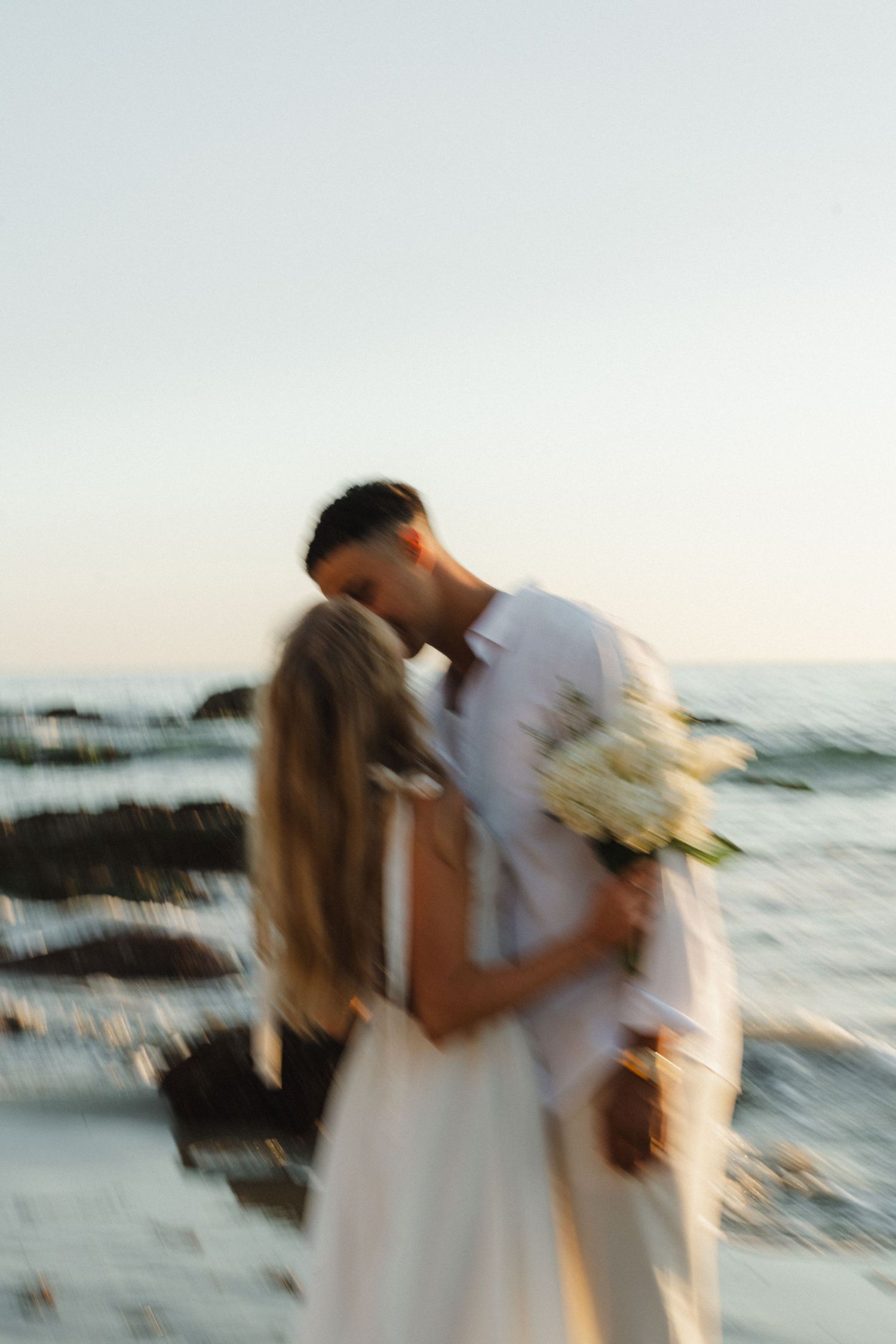 A couple embraces on a rocky beach at sunset in a series of romantic motion-blurred photographs.