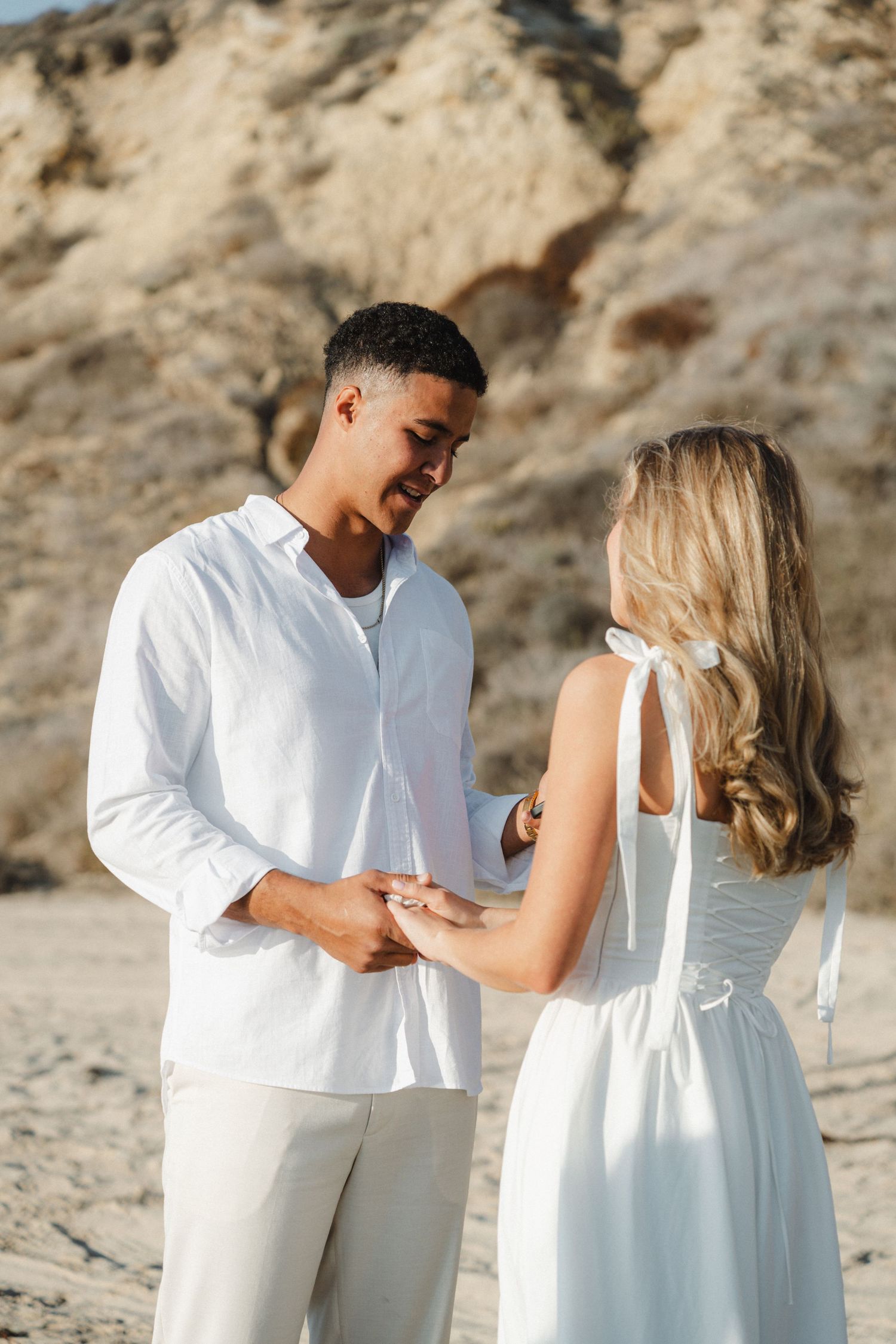 A couple shares intimate moments on a beach, dressed in white wedding attire.