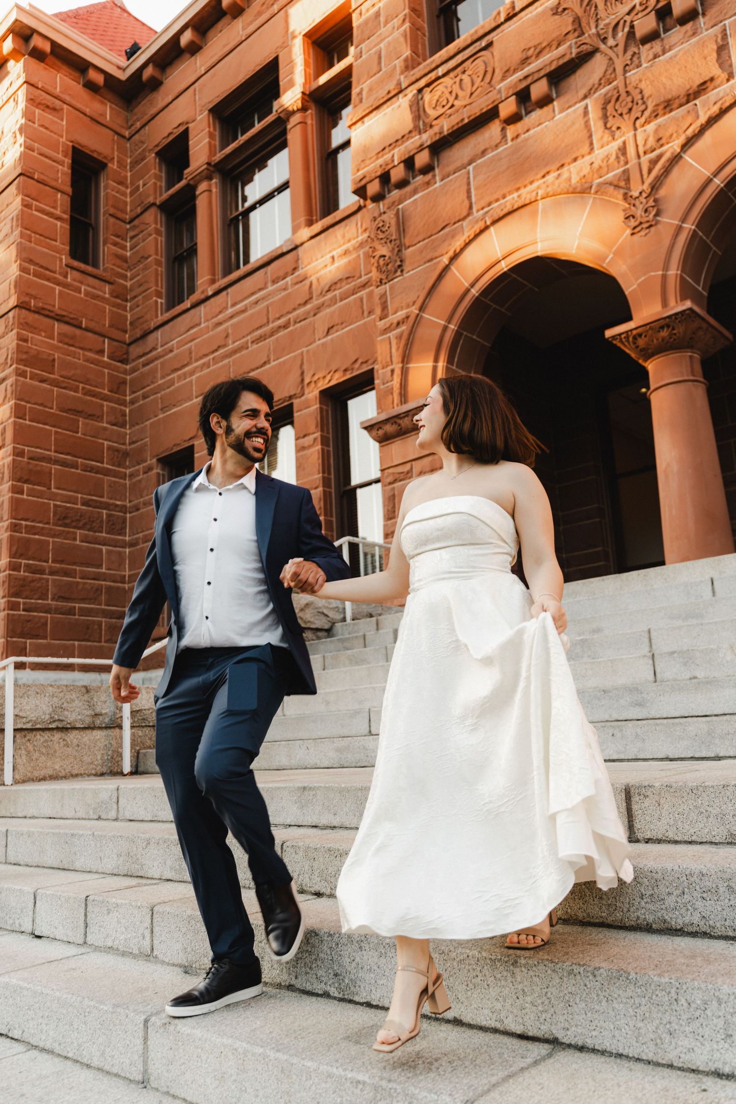 Playful newlyweds dance and twirl on historic brick building steps.