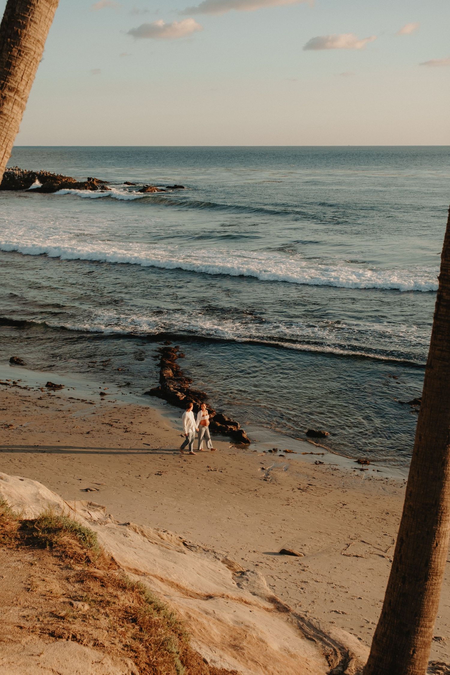 Scenic beach landscape with rocky coastline and gentle waves rolling onto sandy shore at sunset.