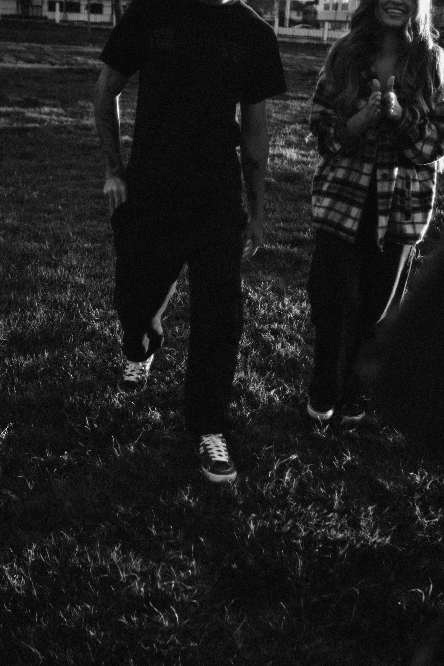 People walking on grass in a dark black and white photograph with shadows cast on the ground.