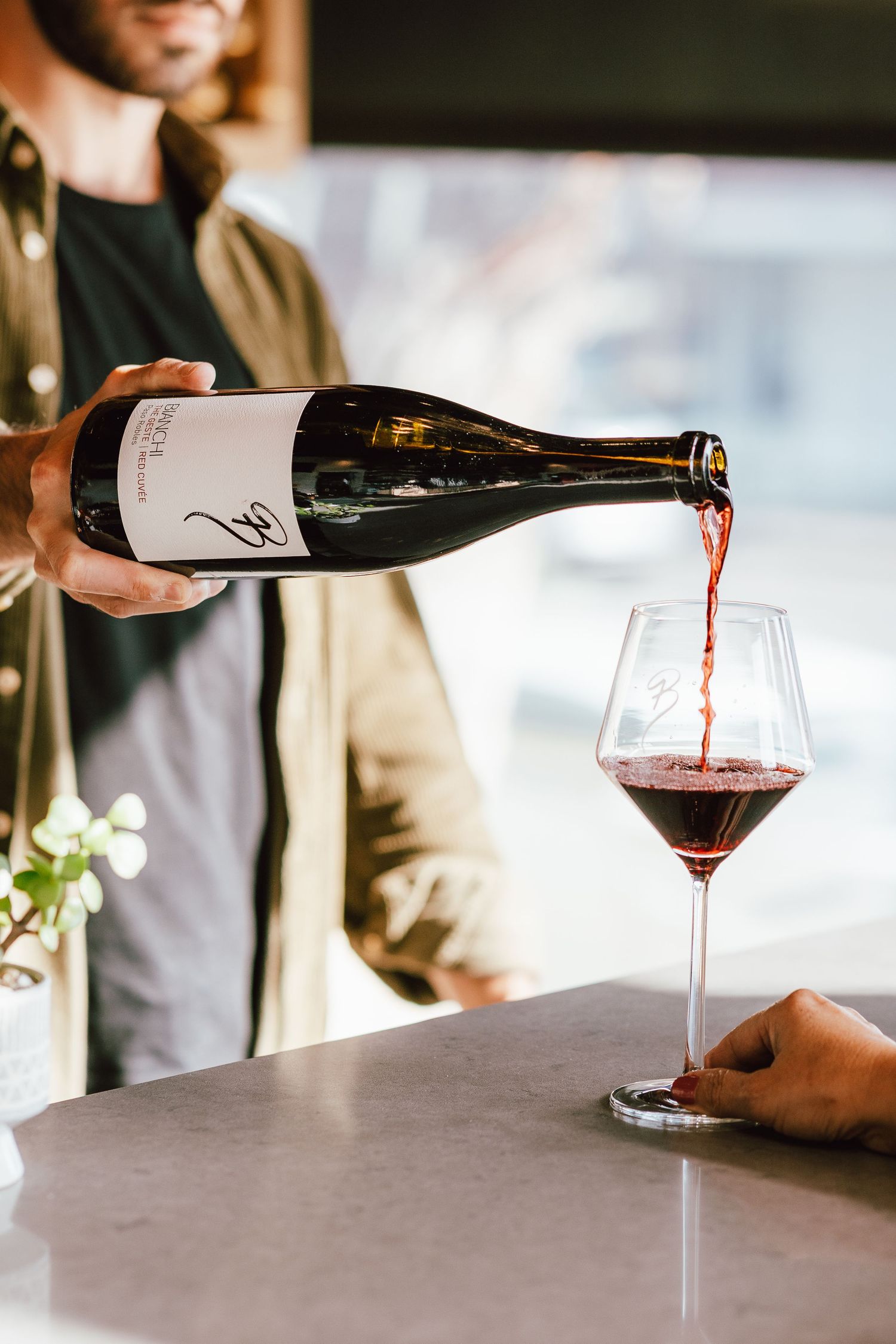 Red wine being poured into elegant wine glasses on a marble countertop.