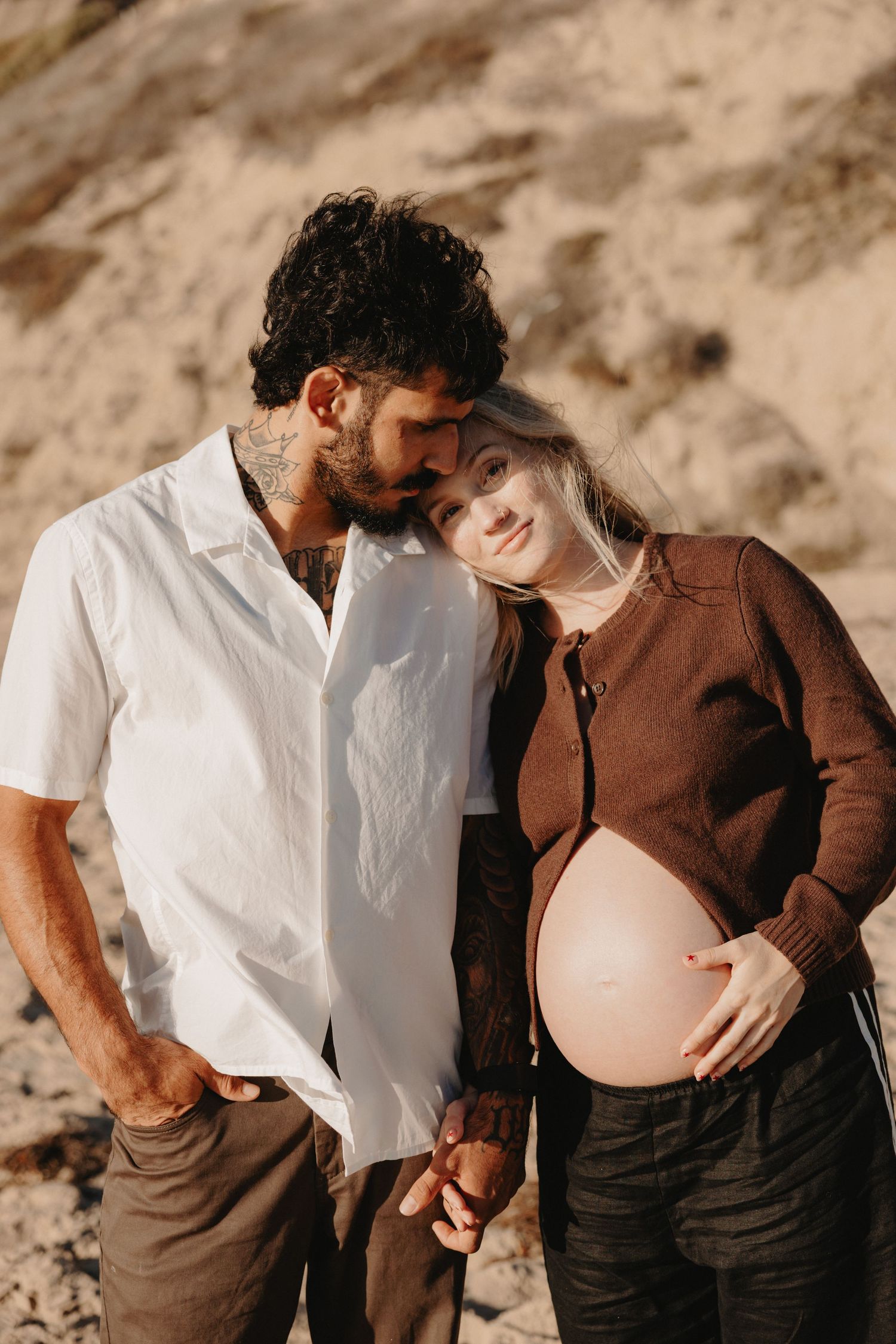A romantic maternity photo series showing a couple in brown and white outfits embracing against a desert backdrop.