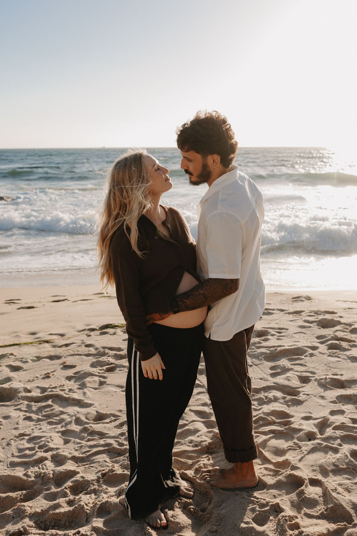 A couple dances together on a sunny beach with ocean waves in the background during golden hour.