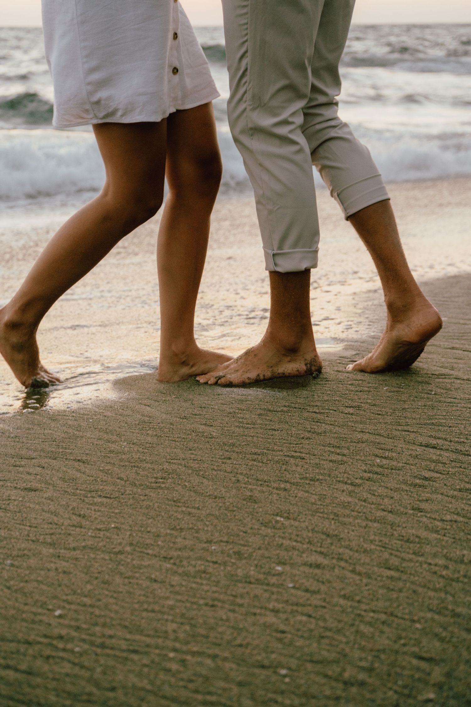 Bare feet of couple standing together on wet beach sand at sunset.