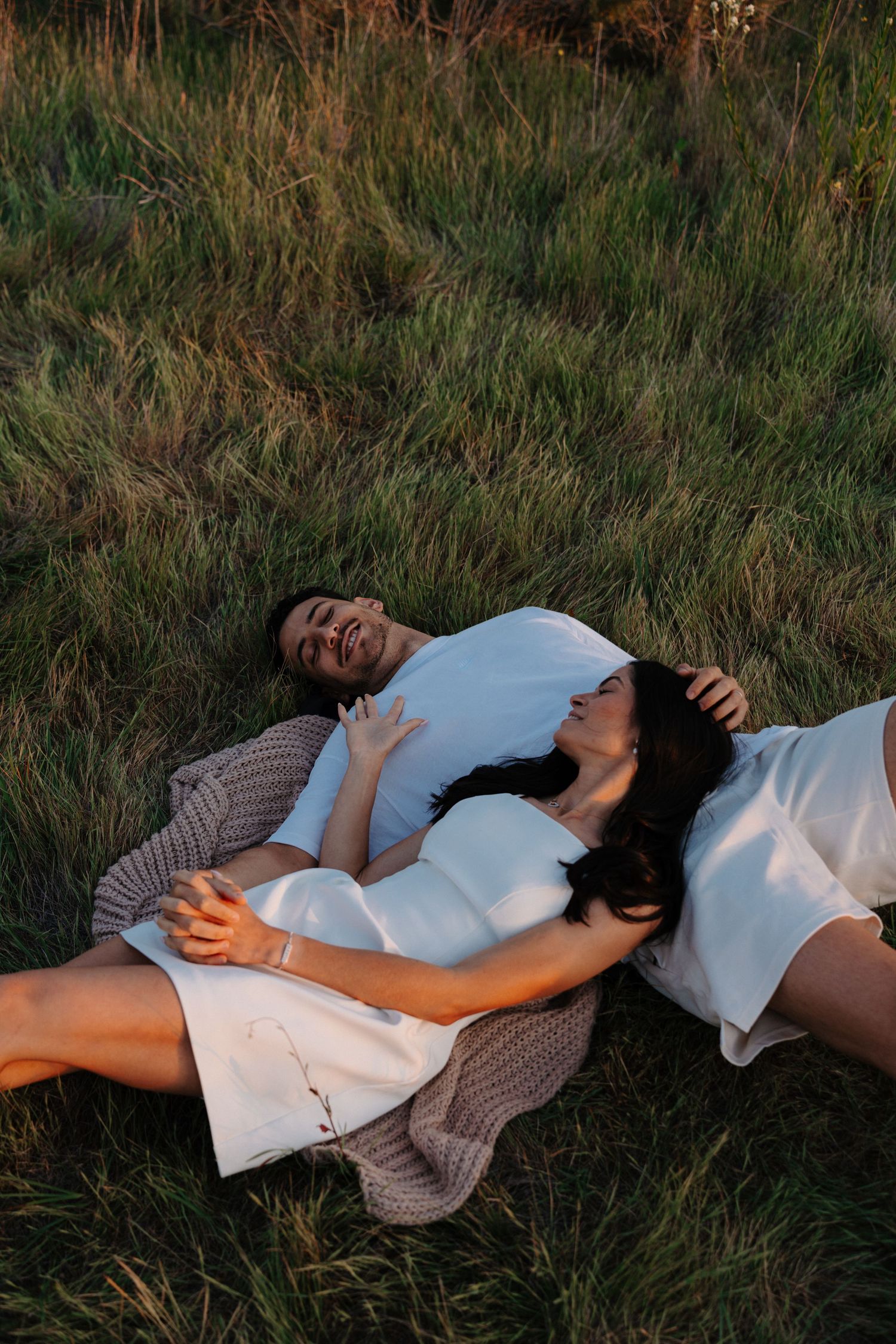 A person in a beige sweater lies peacefully in tall grass at dusk.