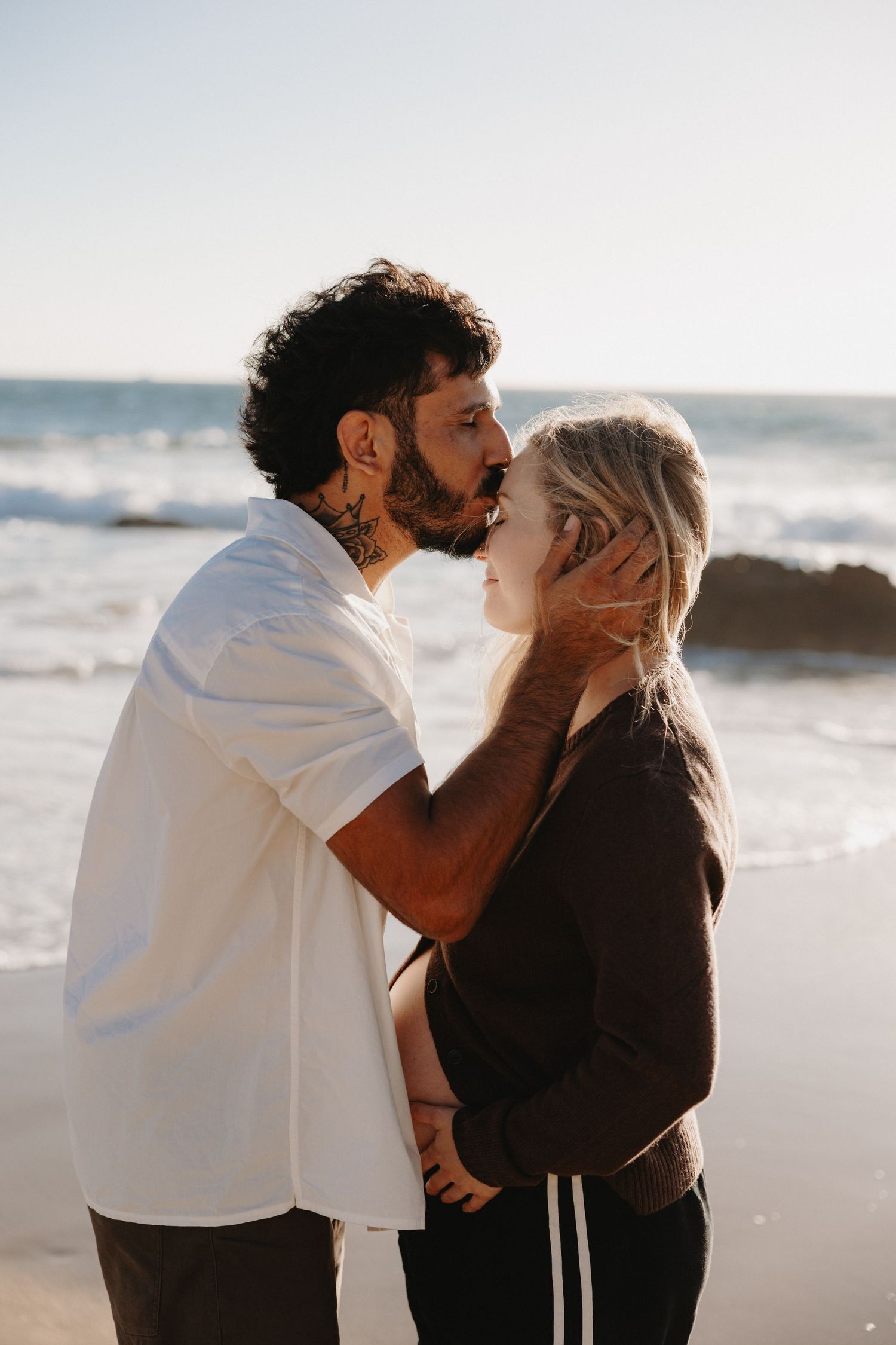 A romantic couple shares tender moments and kisses on a sandy beach at sunset.