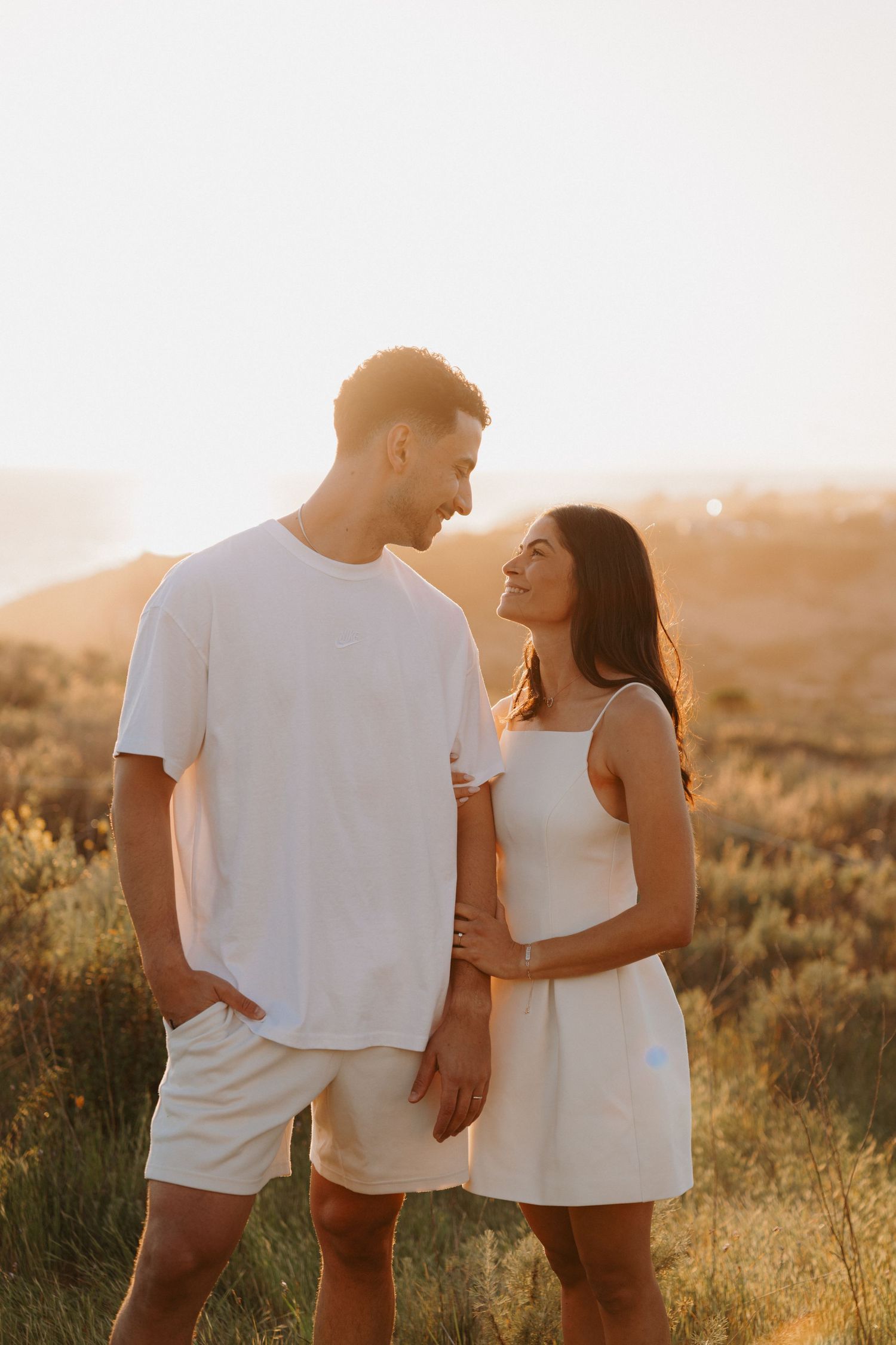 A couple in white outfits sharing a romantic moment at sunset in a golden field.
