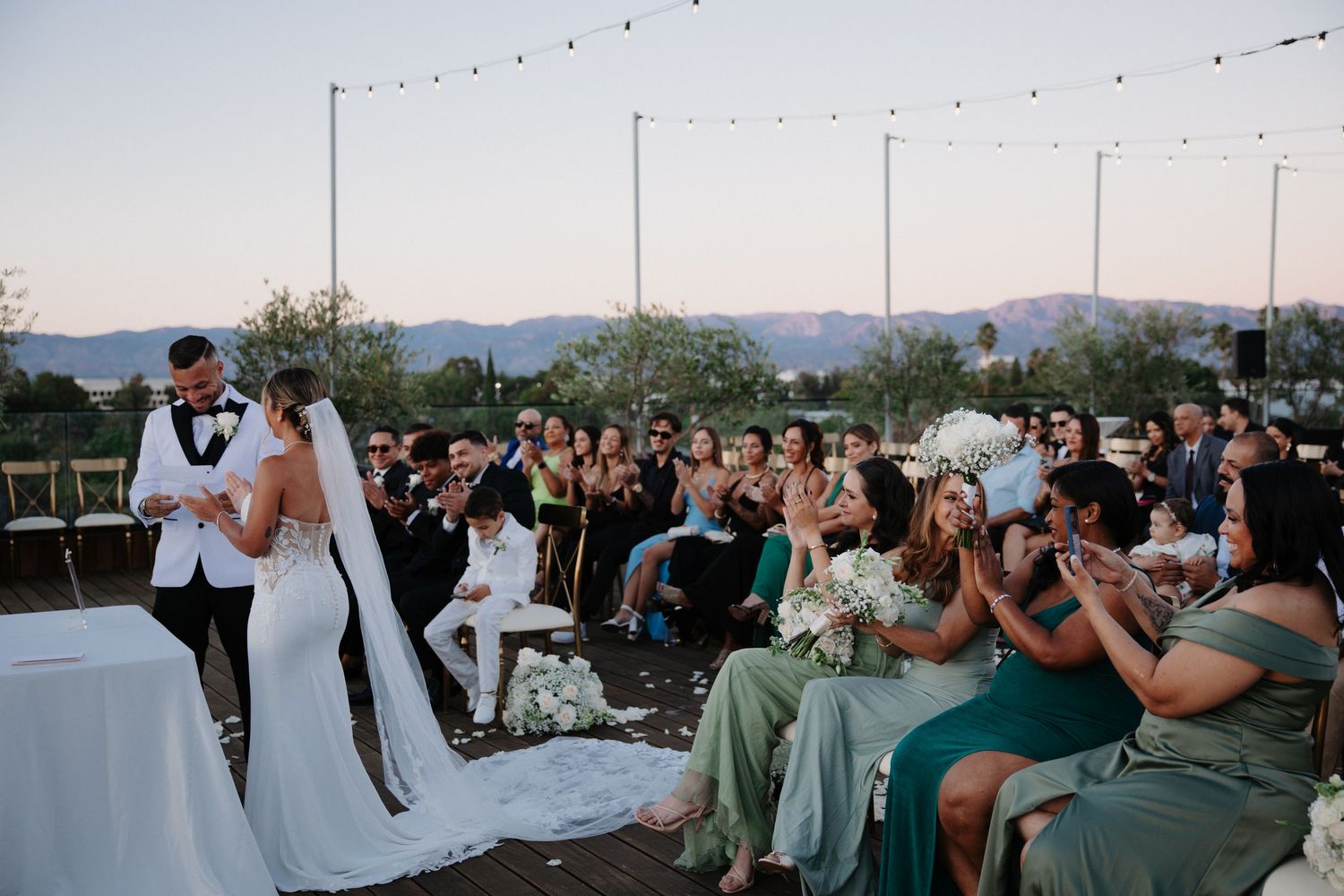 Wedding guests dance and celebrate at an outdoor reception with string lights and mountain views in the background.