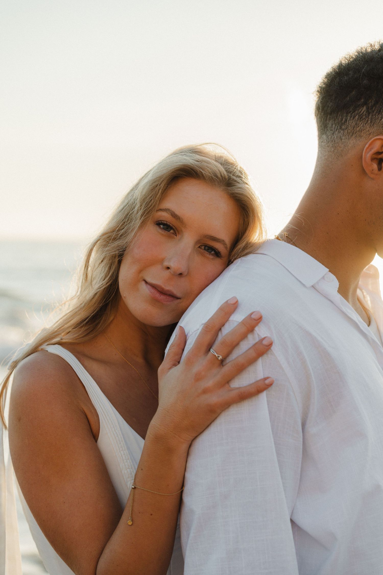 Romantic beach photoshoot series showing tender moments between a couple in white attire against a soft sunset backdrop.