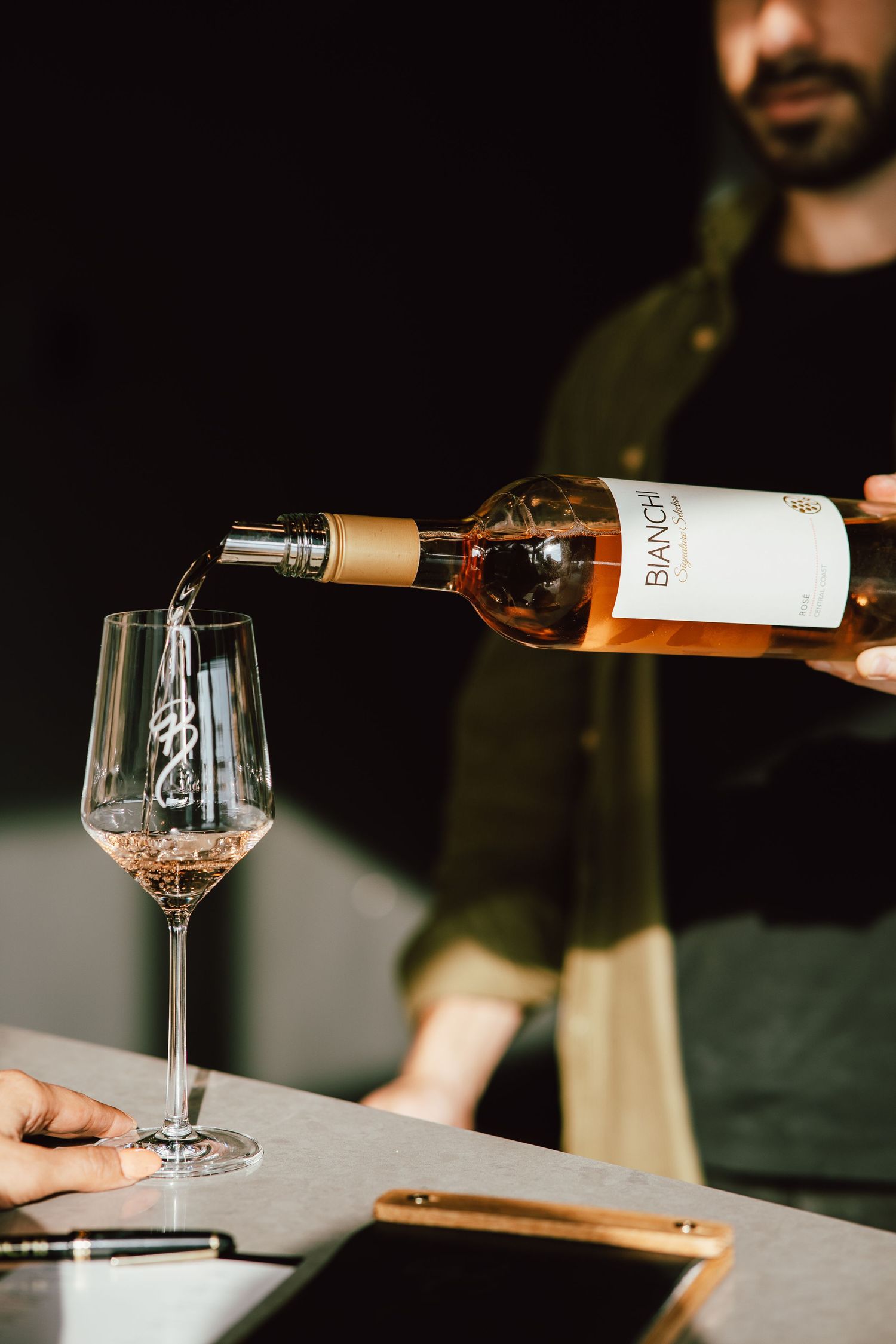 Wine being poured into a glass on a dark table with dramatic lighting.