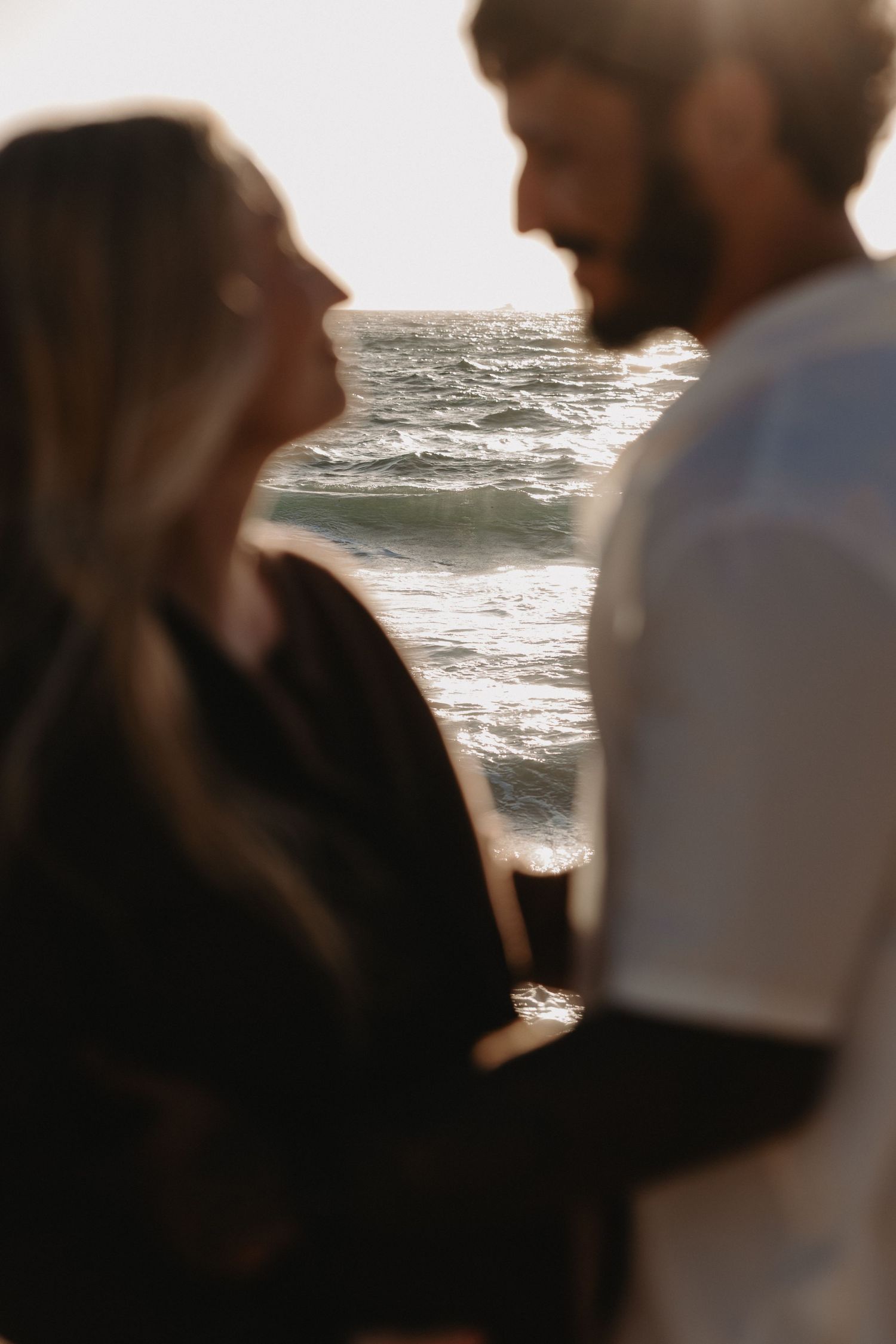 A couple stands silhouetted against the ocean waves during a romantic beach moment at sunset.