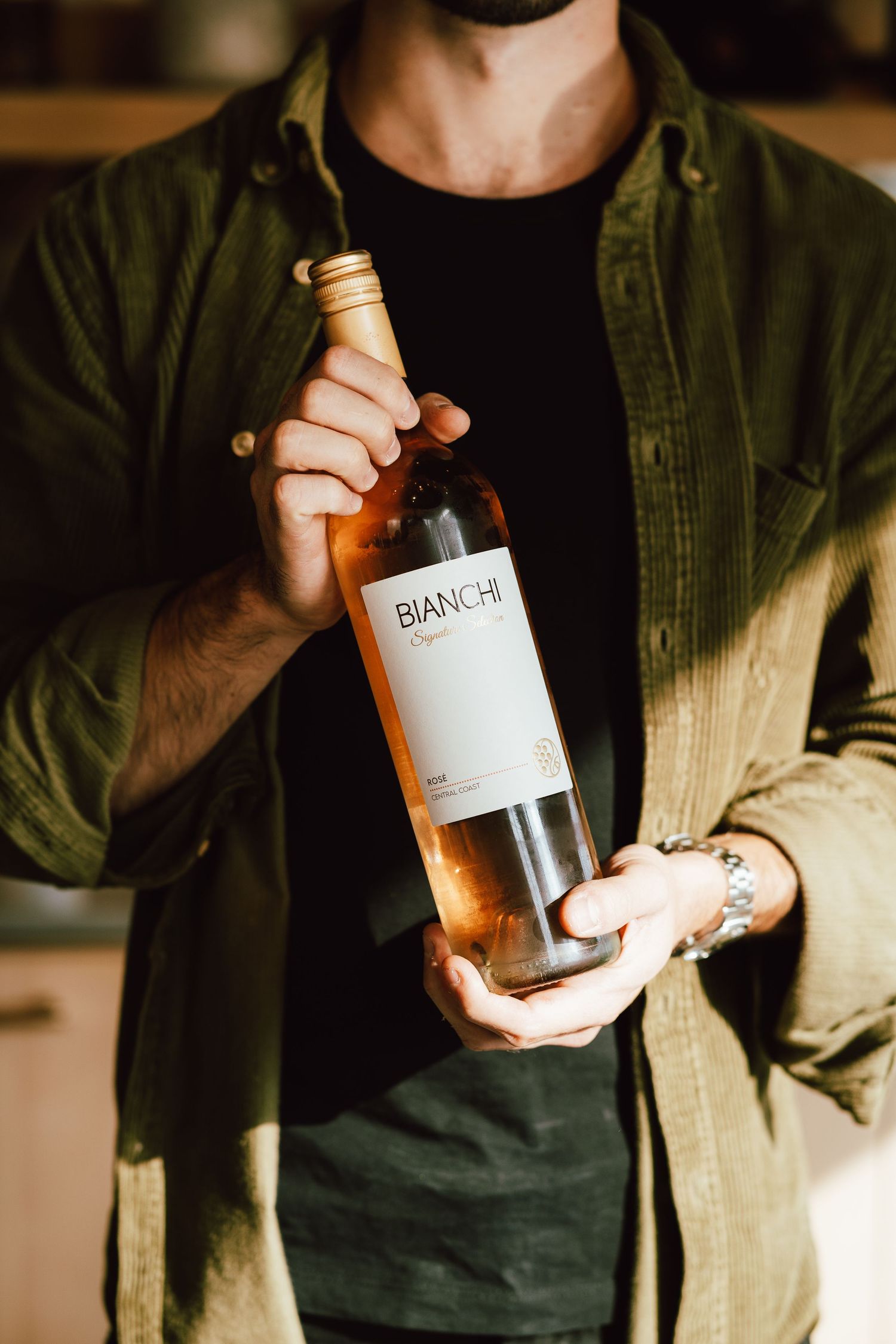 Person in olive jacket holding wine bottle in warm dramatic lighting.