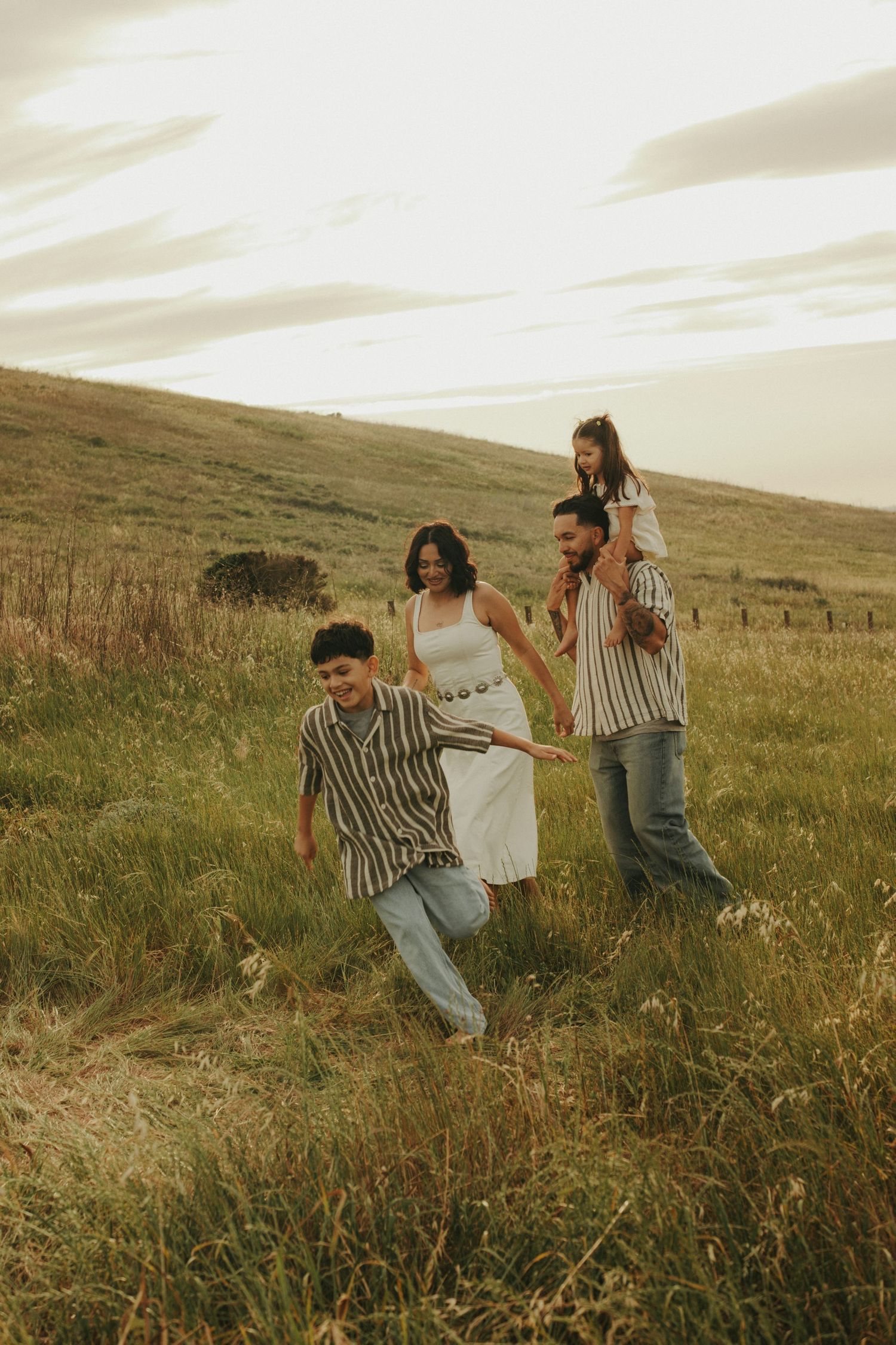 Family of four walking through golden meadow at sunset, parents and two children enjoying outdoor nature stroll.