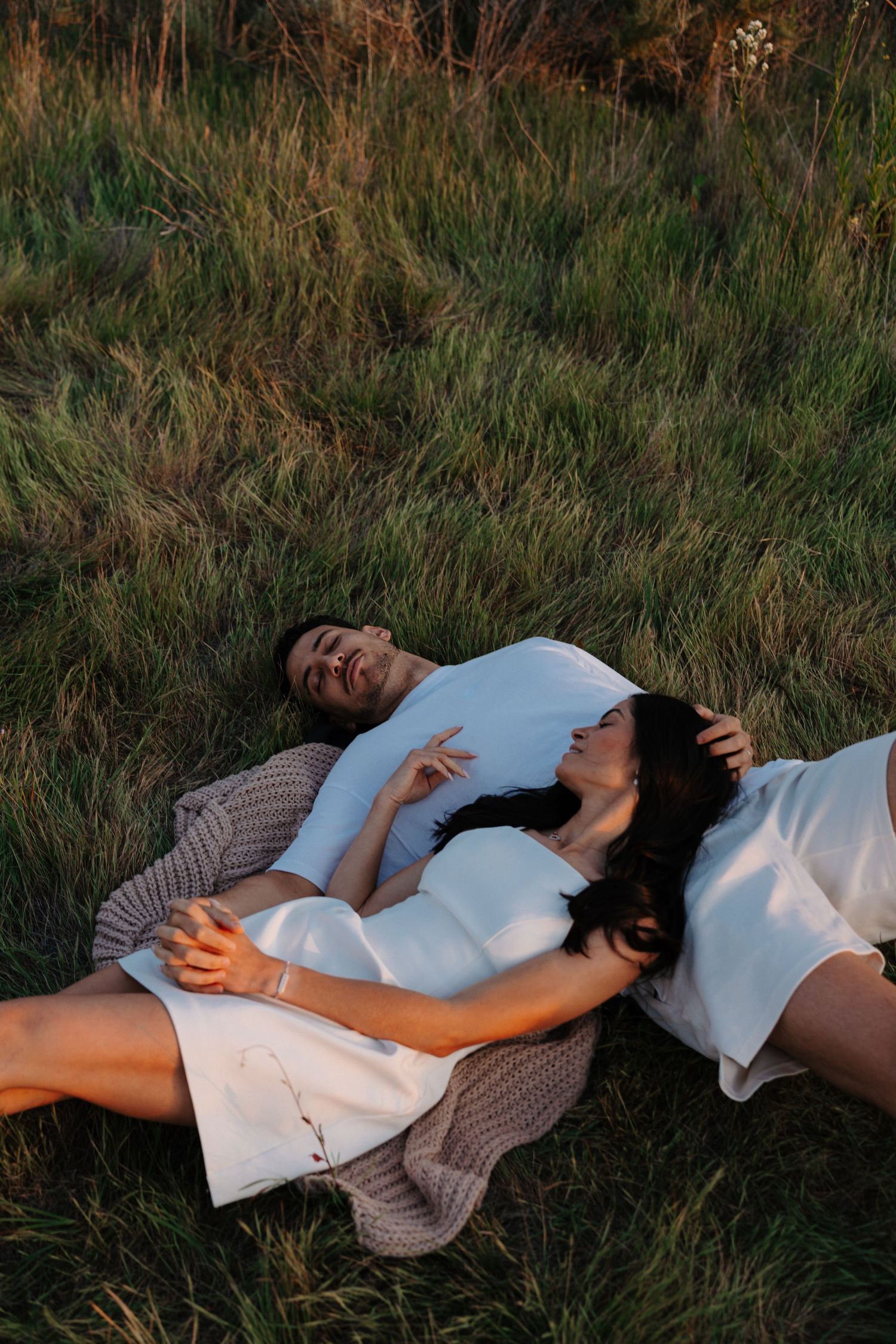 Couple lying in tall grass during sunset photoshoot.