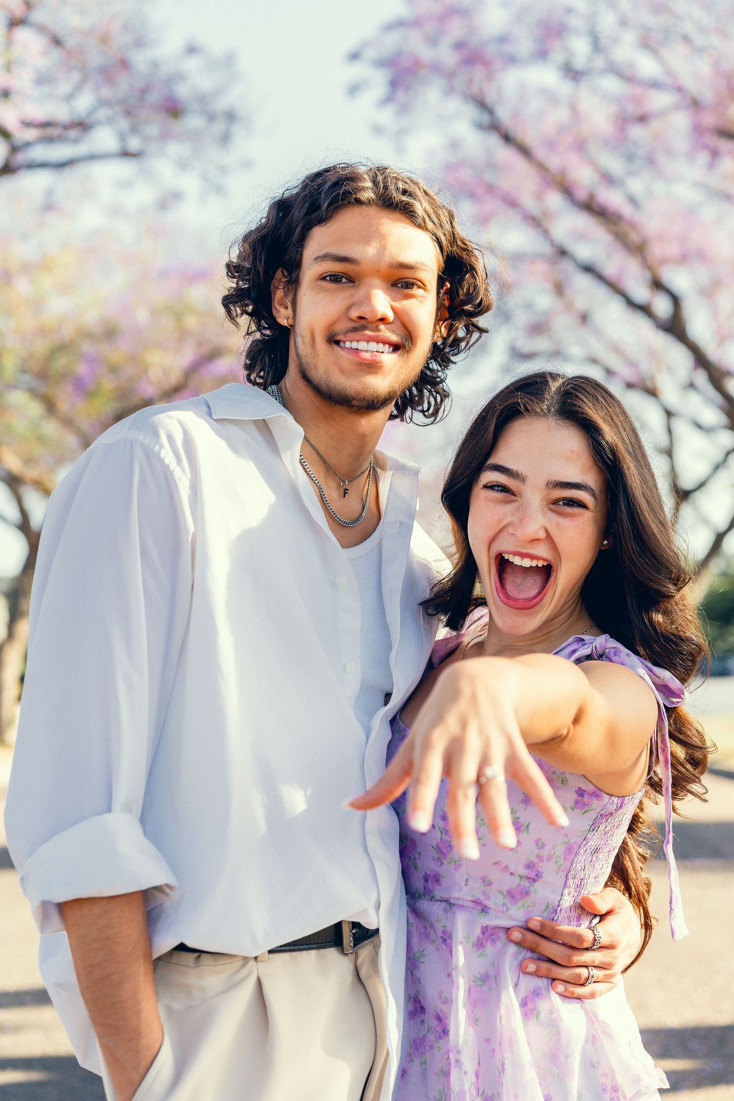A joyful couple celebrating their engagement under flowering trees.