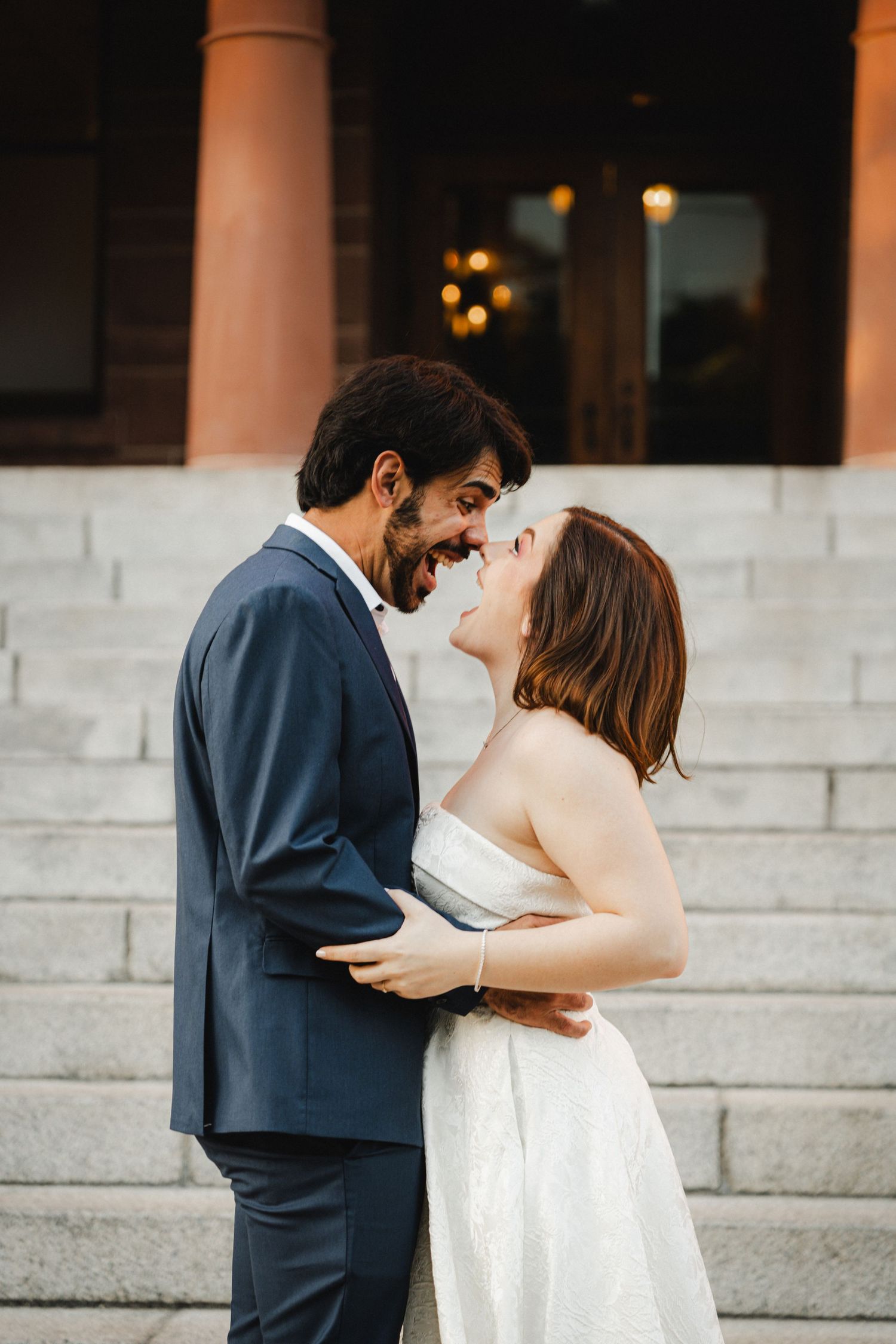 A romantic wedding couple shares an intimate moment on grand stone steps at sunset.