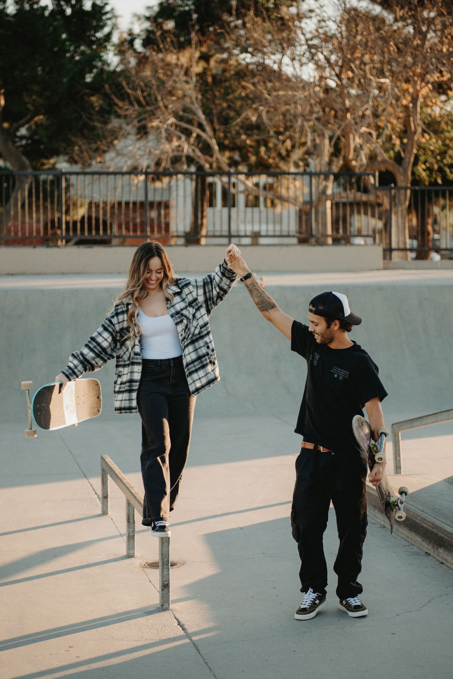 Two skaters practice tricks together at a skate park during golden hour with long shadows on the concrete.