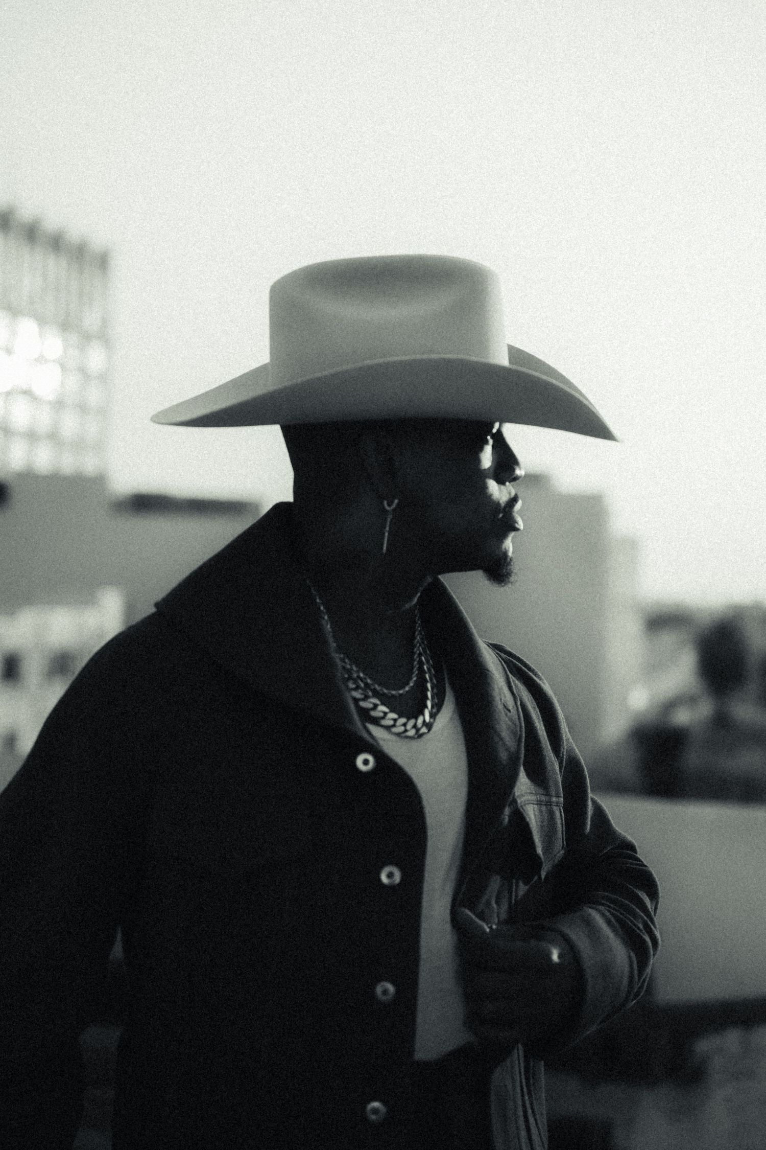 Stylish figure in black wearing cowboy hat captured in dramatic black and white portrait.