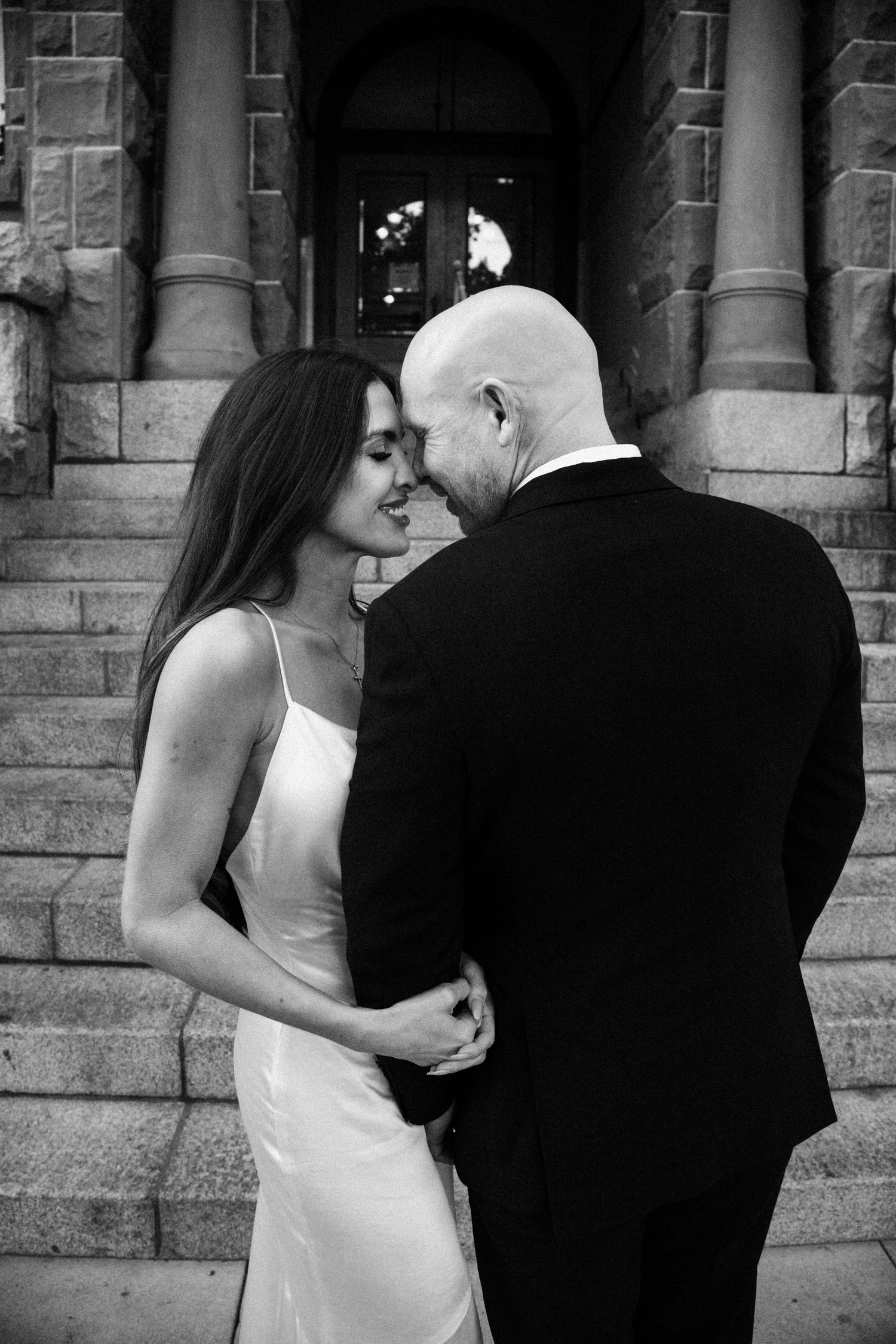 A black and white wedding photo sequence showing a couple in formal attire embracing against a stone building exterior.