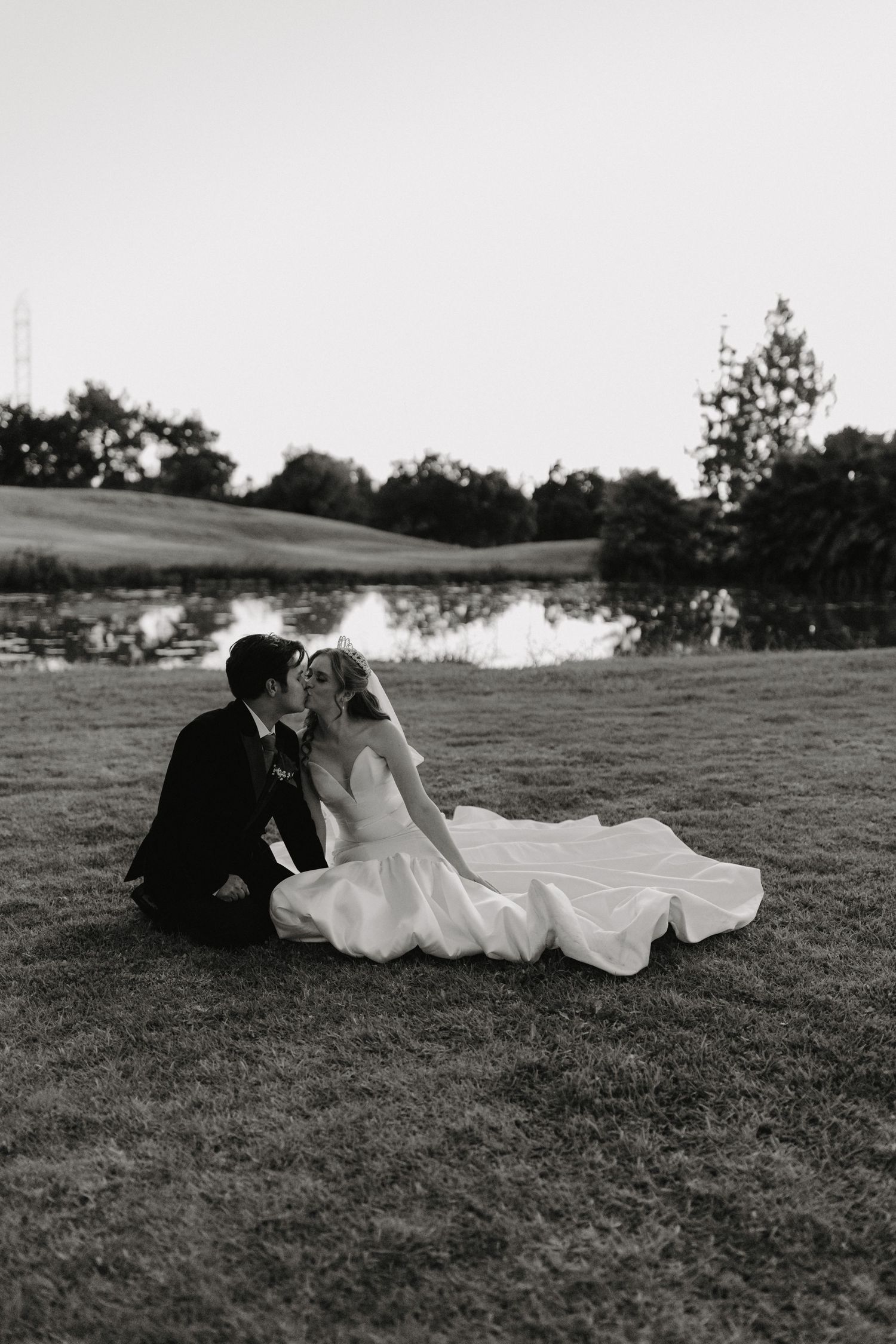 A romantic black and white photo series of a couple sitting together on a grassy hillside in formal attire.