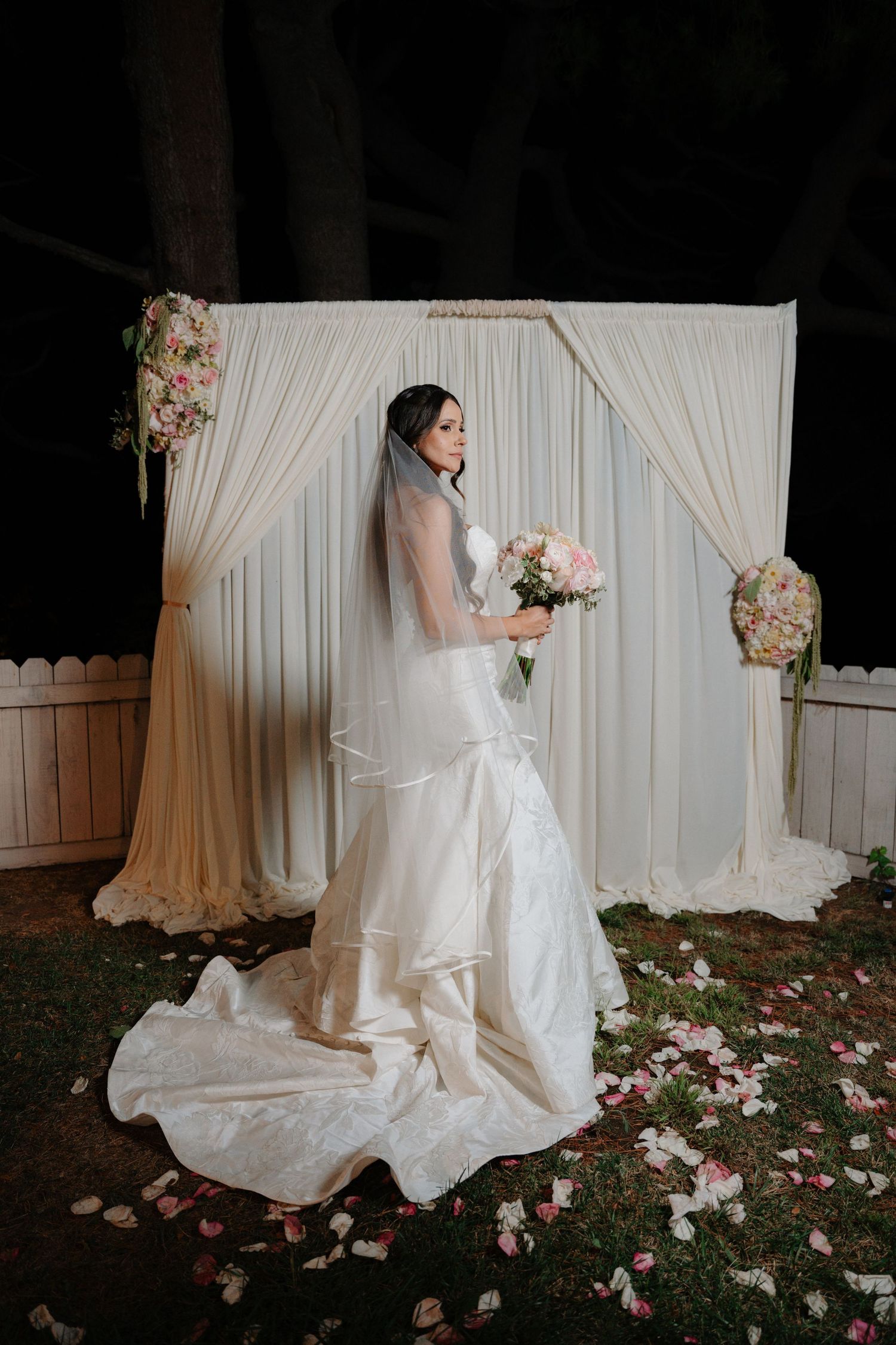 A series of romantic bridal portraits showing a white wedding dress against a draped backdrop with scattered rose petals.