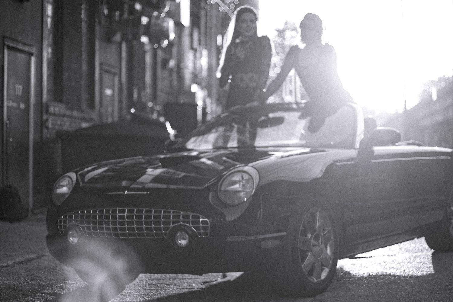 Classic car silhouetted against bright sunlight in urban setting.