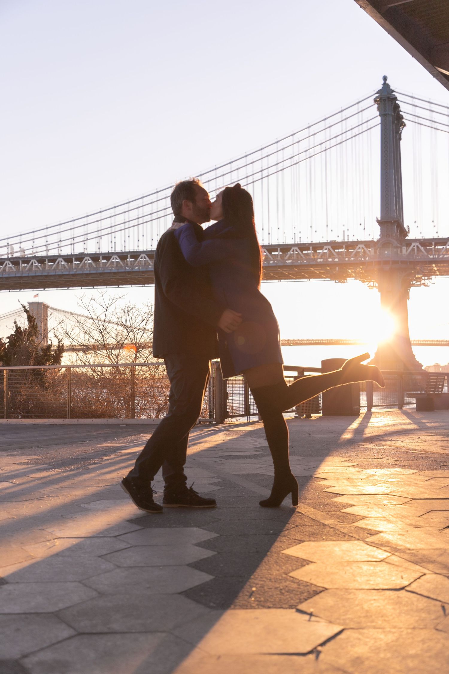 Silhouettes dancing near a bridge at sunset create romantic shadows on the ground.