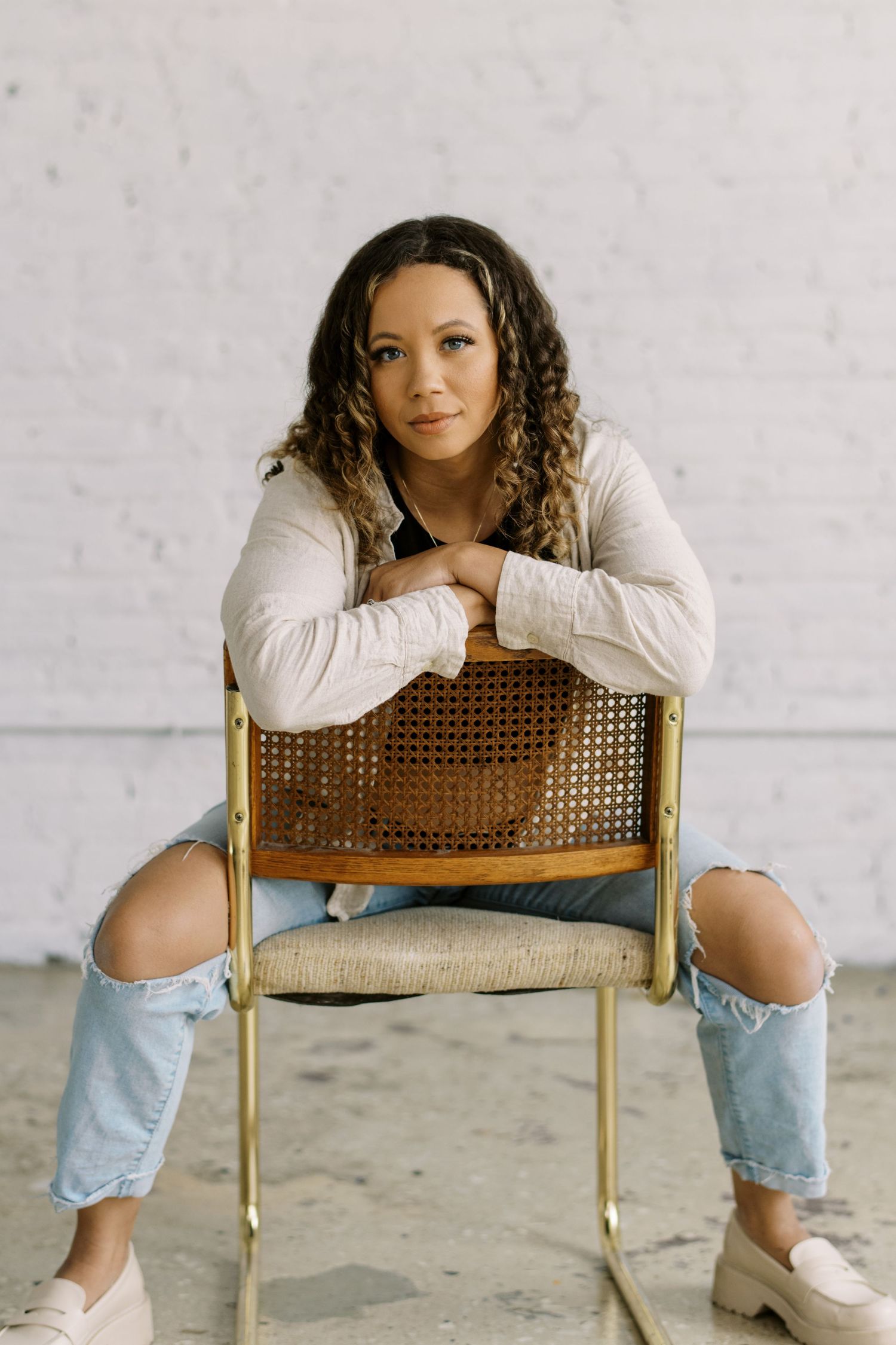 Person sitting casually on a vintage cane chair wearing distressed jeans.