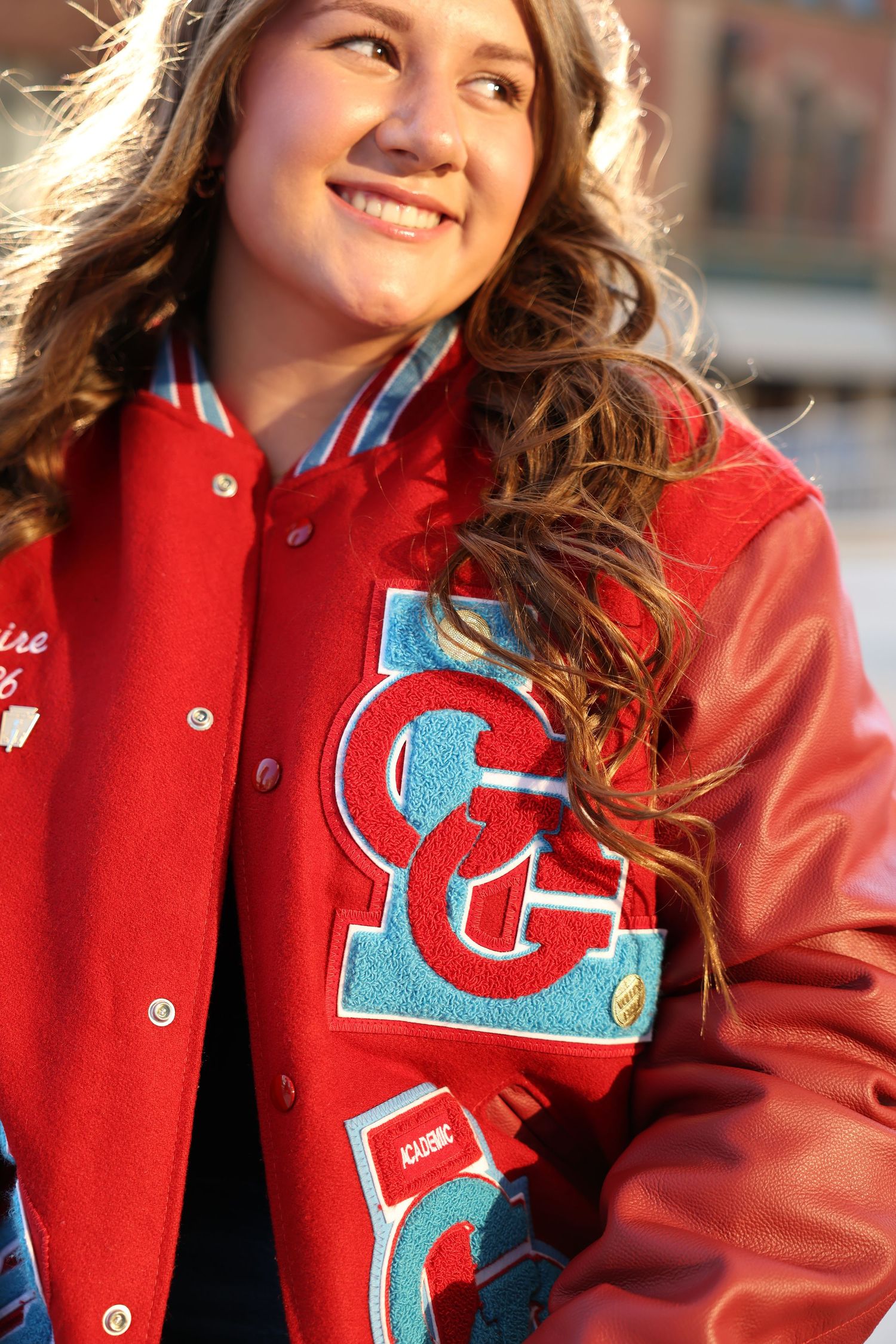 Person wearing red varsity letterman jacket with blue lettering in golden sunlight.