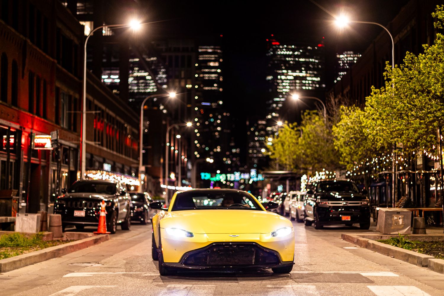Nighttime city street with yellow sports car and urban buildings.