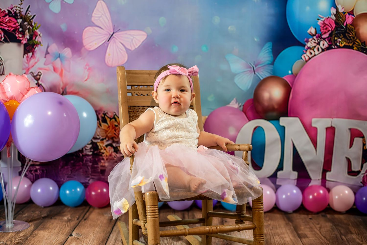 Baby girl's first birthday setup with pink and blue balloons, butterflies, and dreamy backdrop.