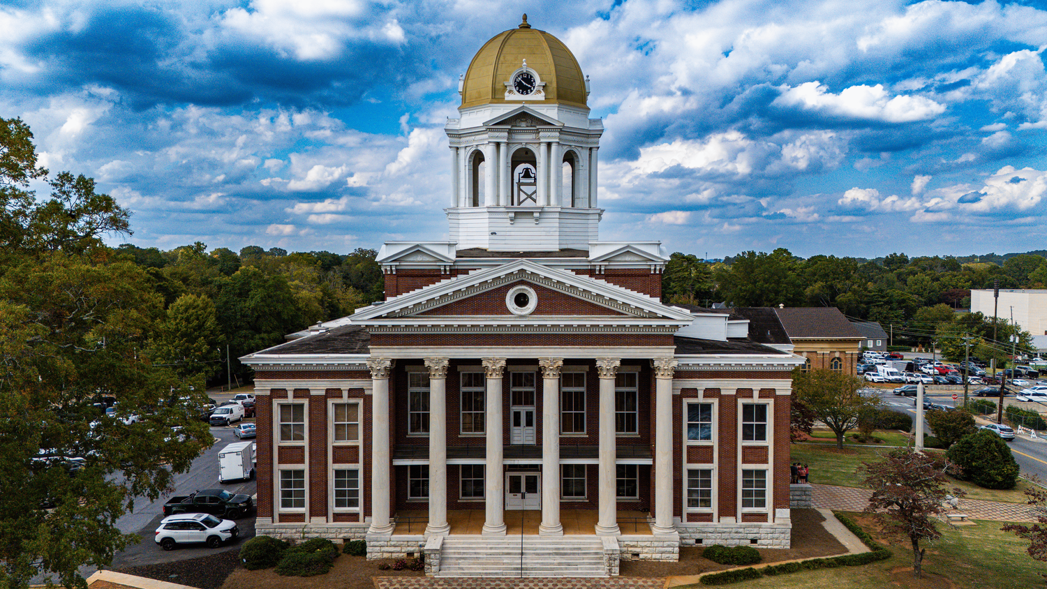 A series of historic colonial buildings with white columns and domed cupolas against blue skies with puffy clouds.