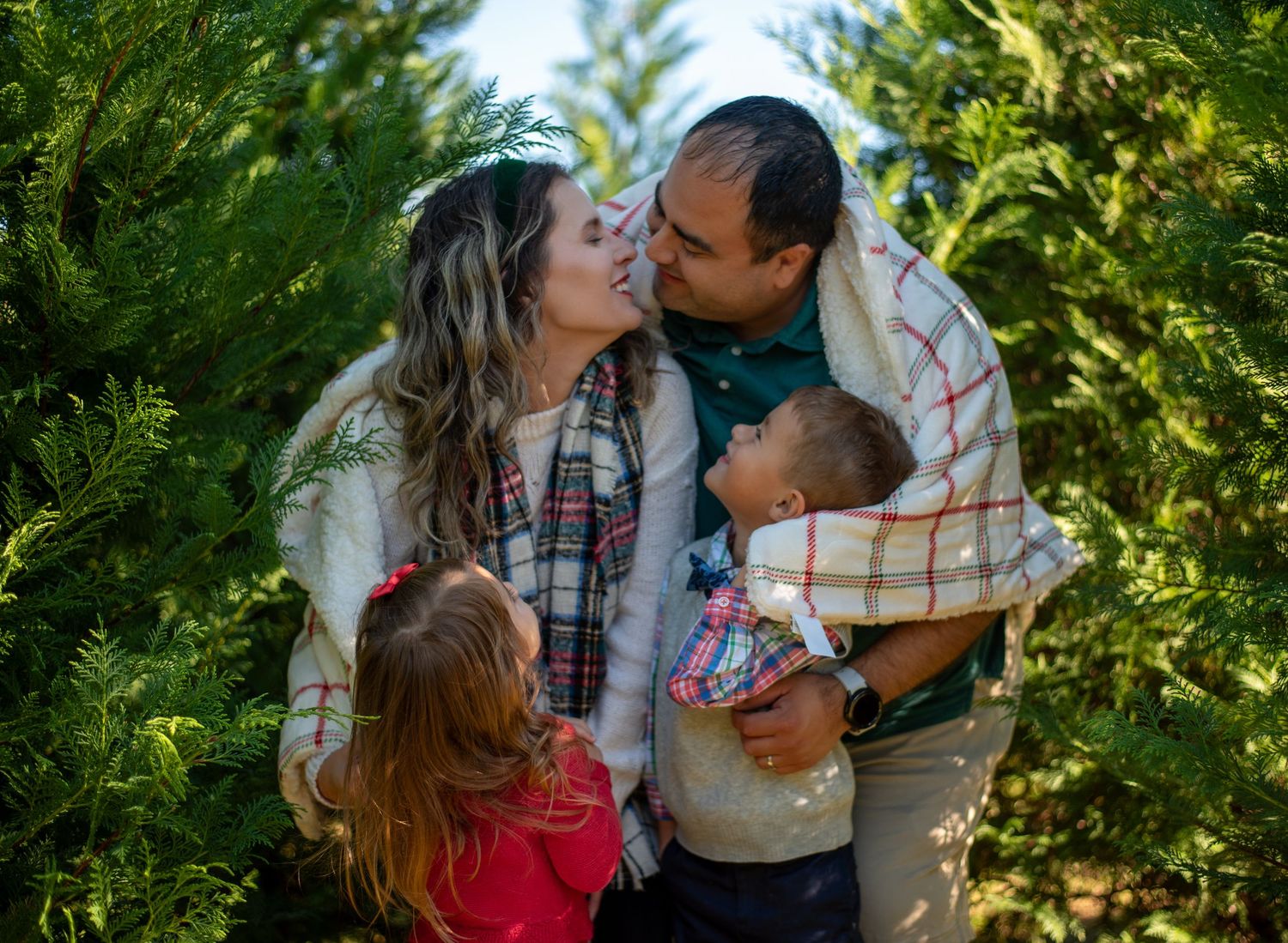 A loving family moment captured in a lush green pine tree setting.