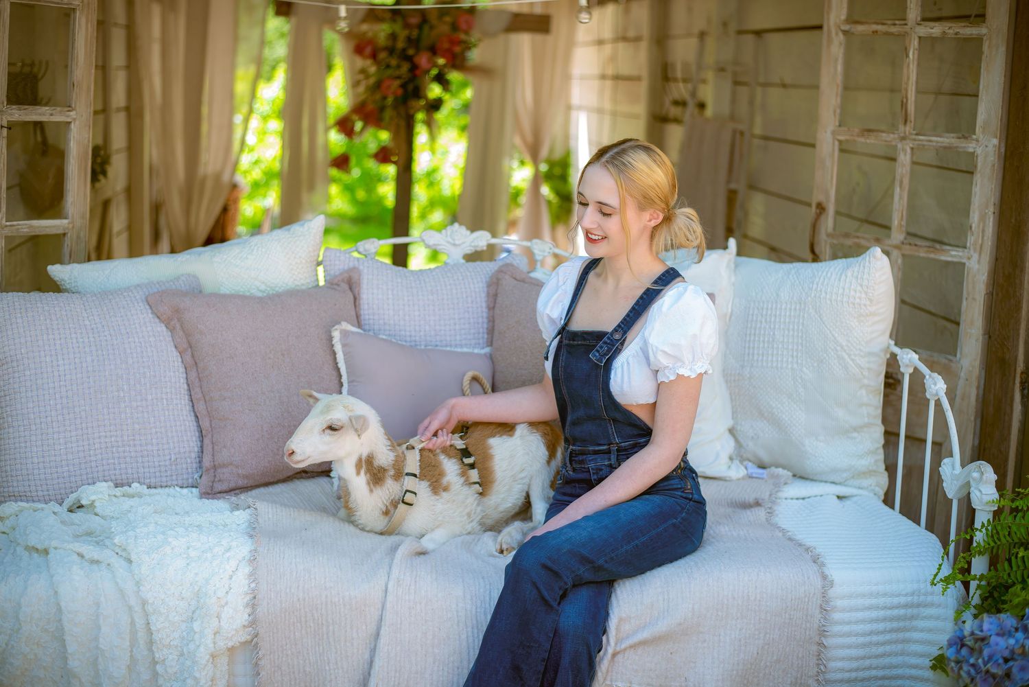 A person relaxes on a white couch with a white baby goat on a sunny afternoon.