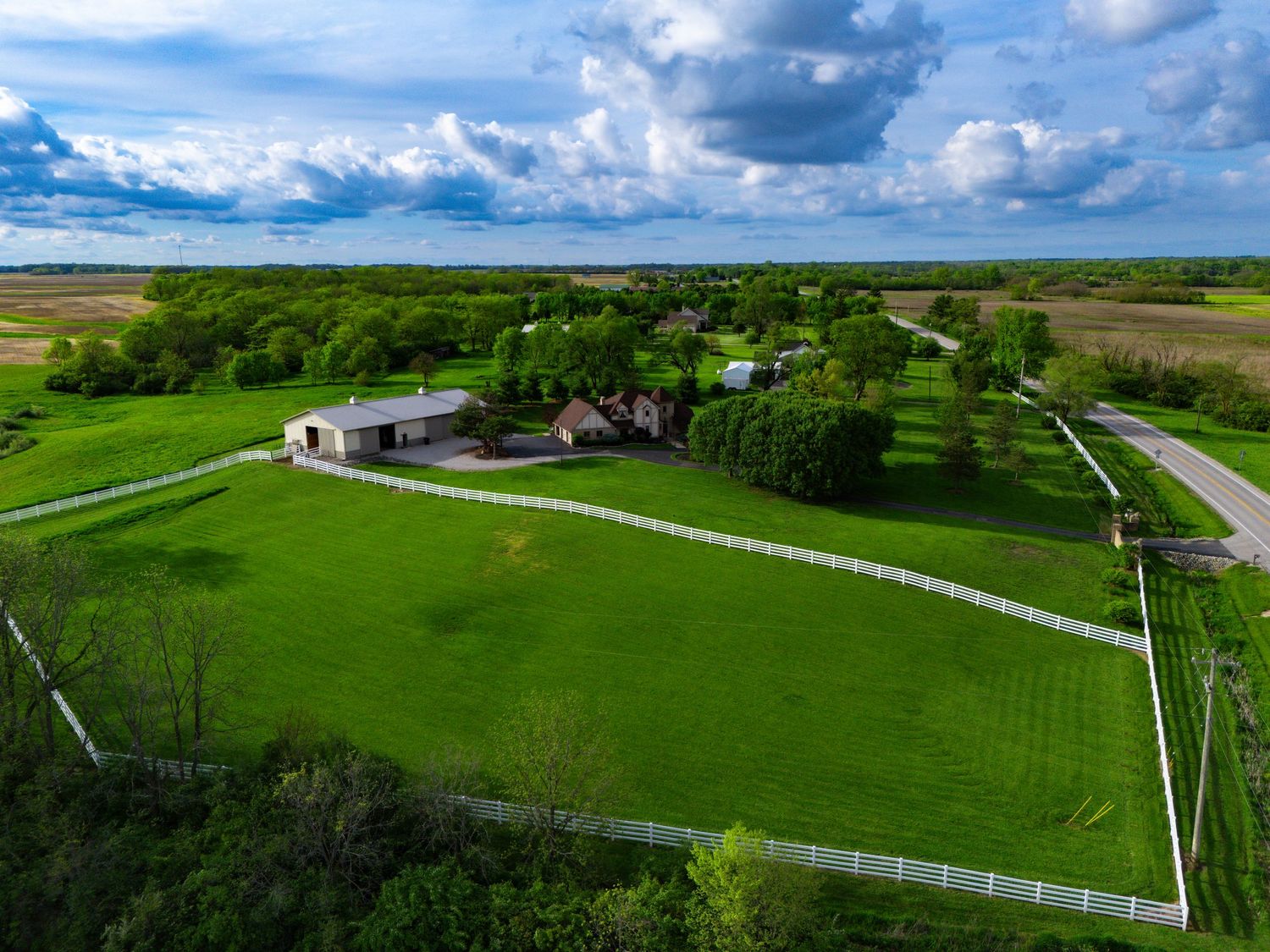 Aerial panorama of a lush green farm with white fences, driveways, and buildings under a dramatic cloudy sky.