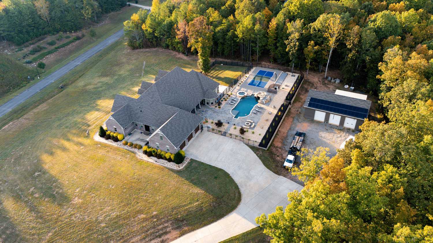 Aerial view of residential neighborhood with autumn trees, swimming pool and winding roads during golden hour.