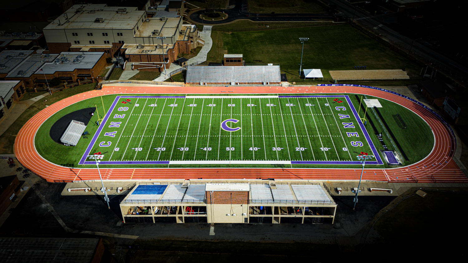 Aerial view of high school football stadium with green turf field and running track.