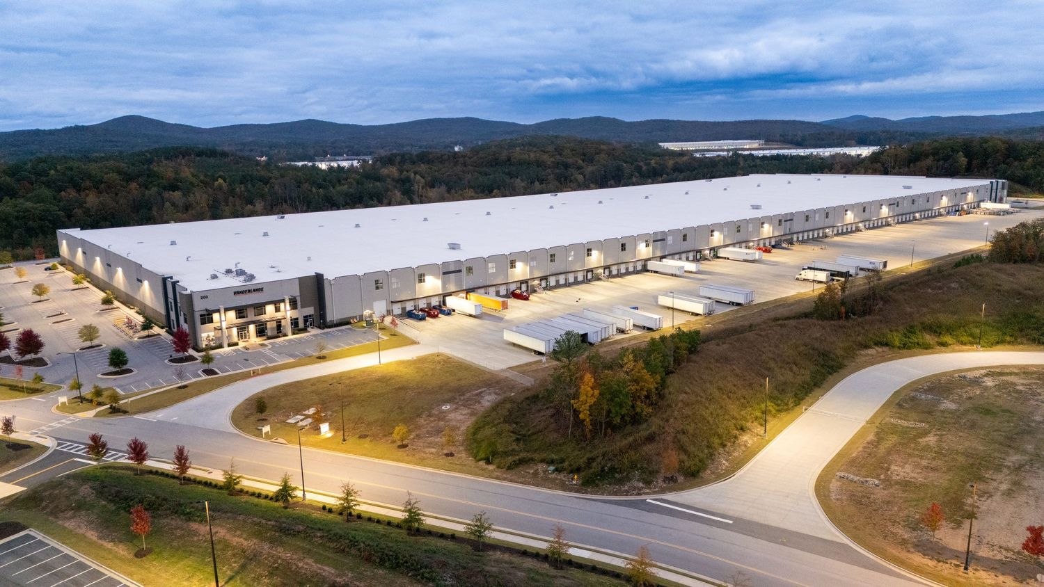 Aerial view of a large white industrial warehouse building with loading docks and surrounding roads in a rural area.